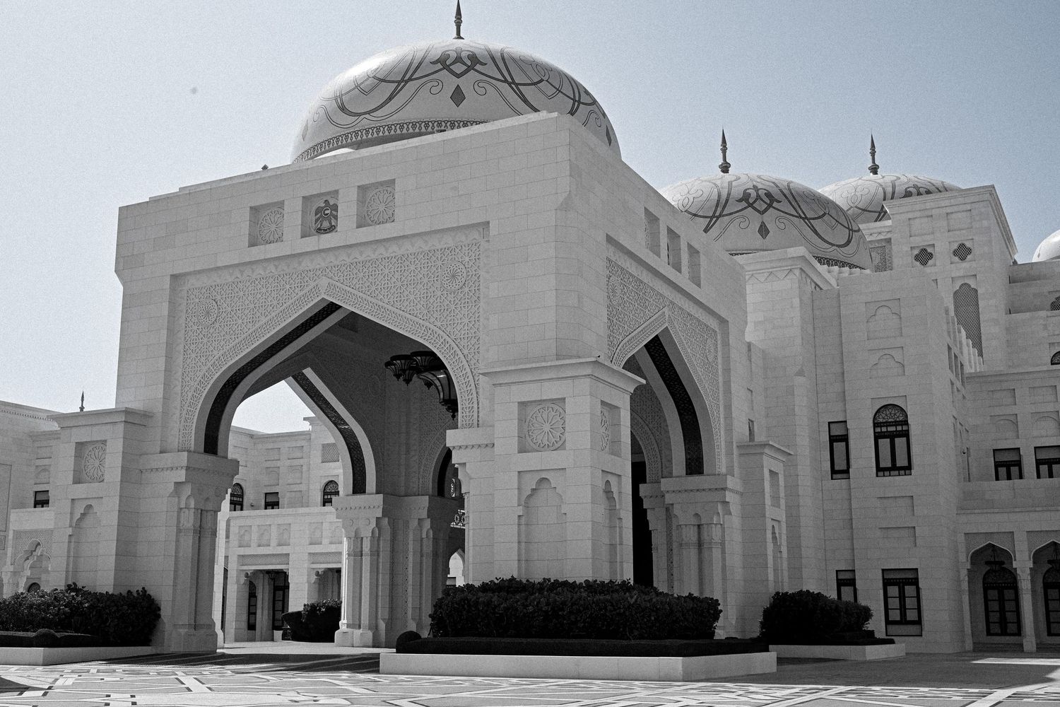 Exterior view of grand mosque with white domes and arched entrances.