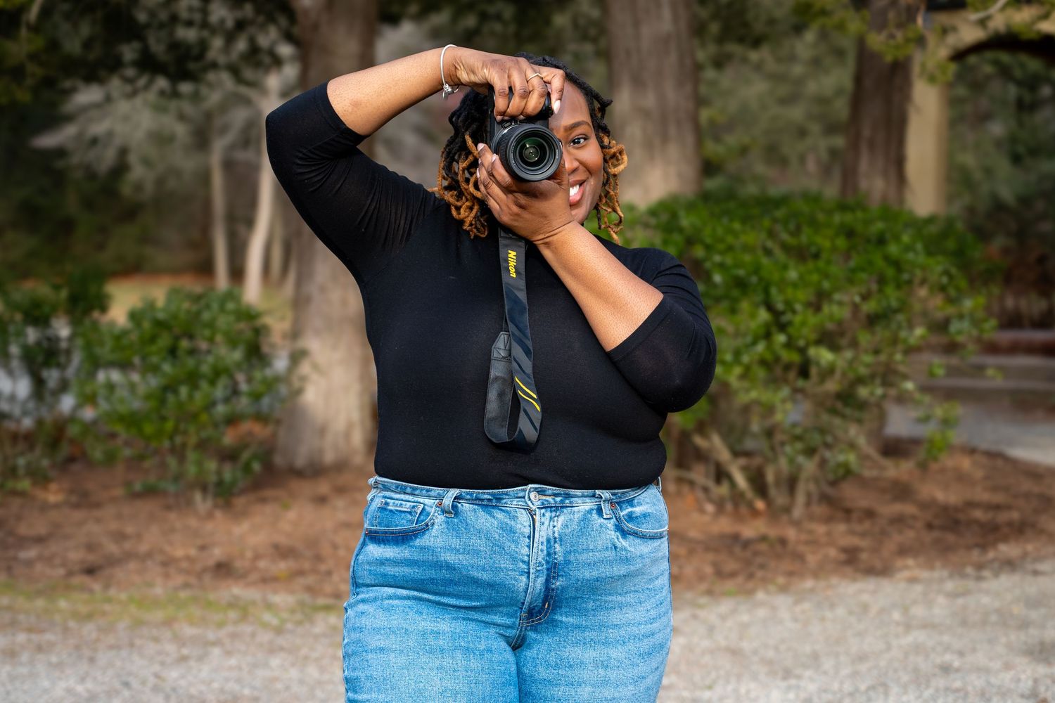 Photographer holding camera while standing on outdoor path with trees in background.
