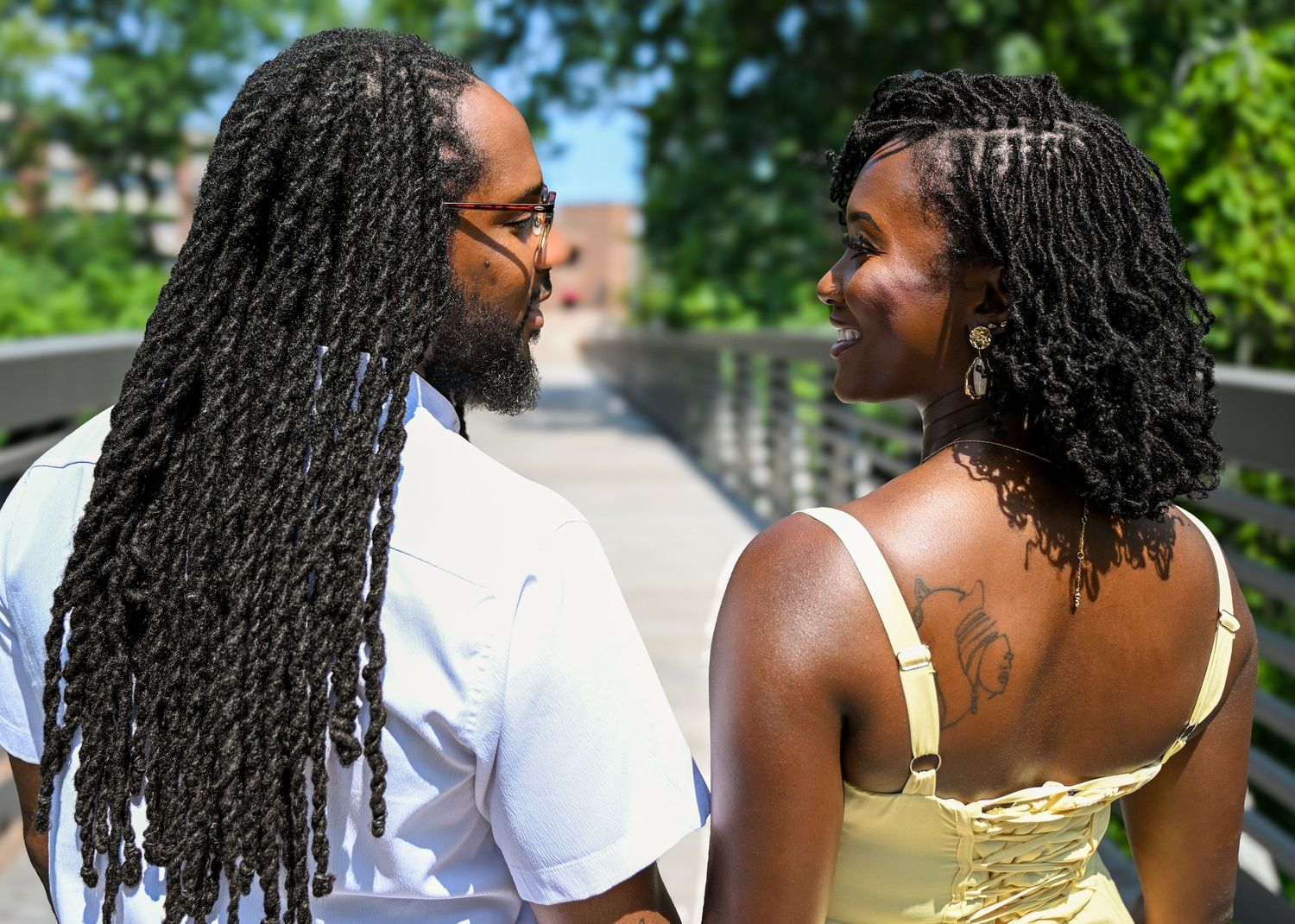 Two people with braided hairstyles share a joyful moment together outdoors on a sunny day.