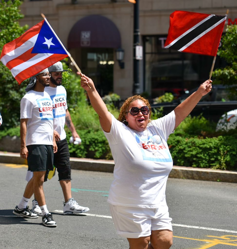 Parade participants wave Puerto Rican and Trinidad & Tobago flags during a festive street celebration.