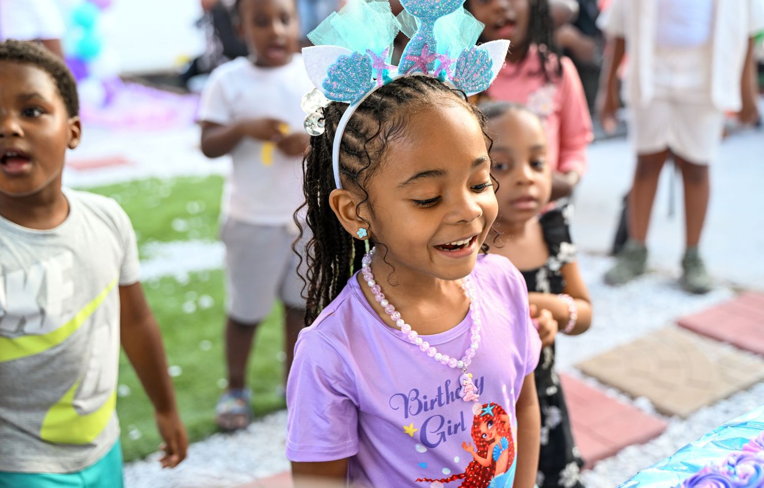 Children playing outdoors at a party with blue balloons and decorations.