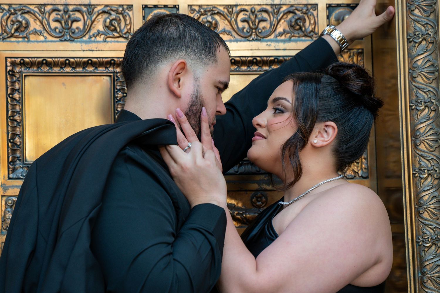 Elegant couple embracing in front of ornate gold-framed backdrop.