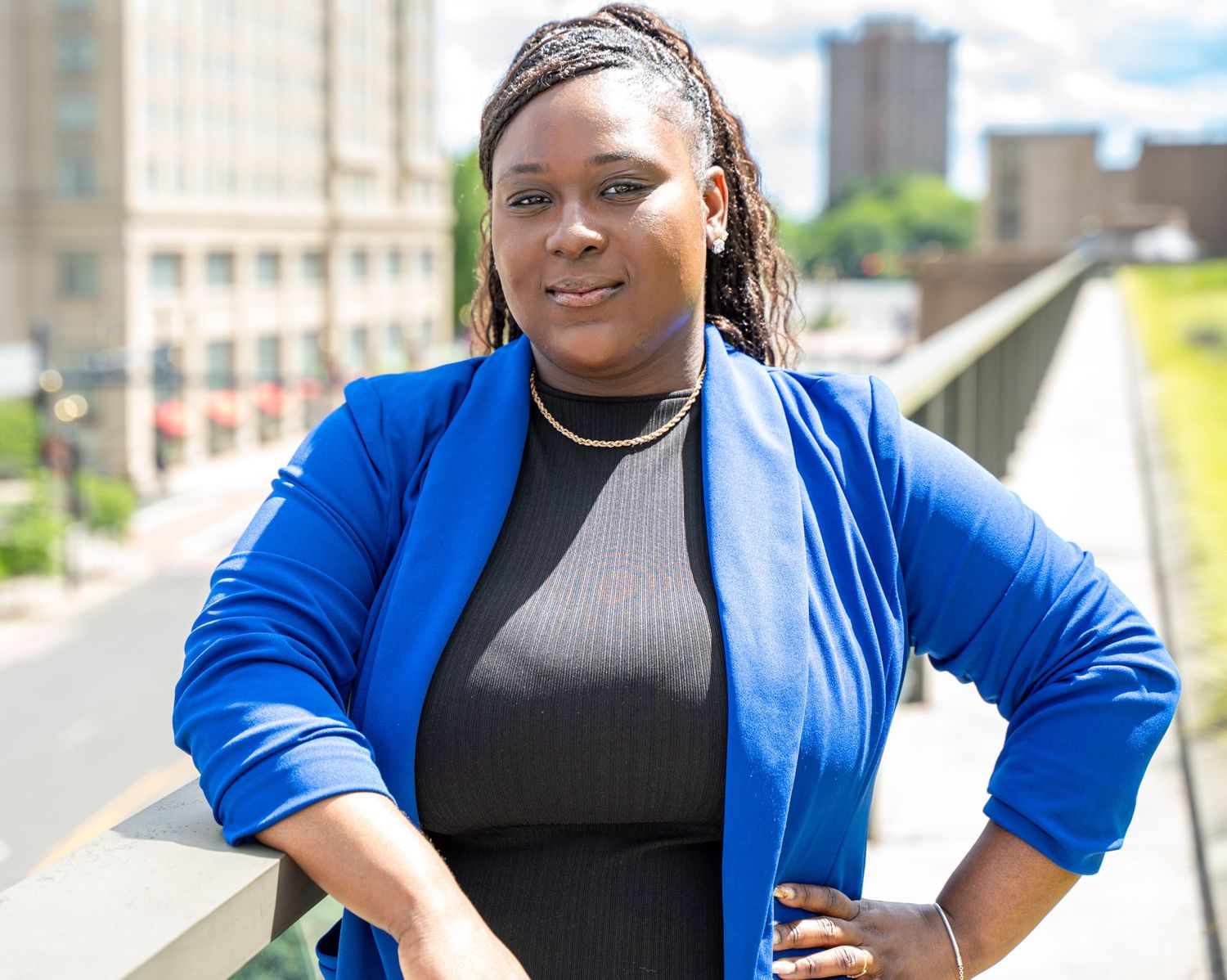 Portrait of person in bright blue blazer and black top posing on urban bridge.