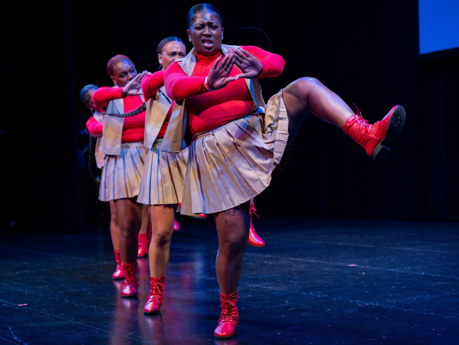 Dancers in red costumes performing on a dimly lit stage.