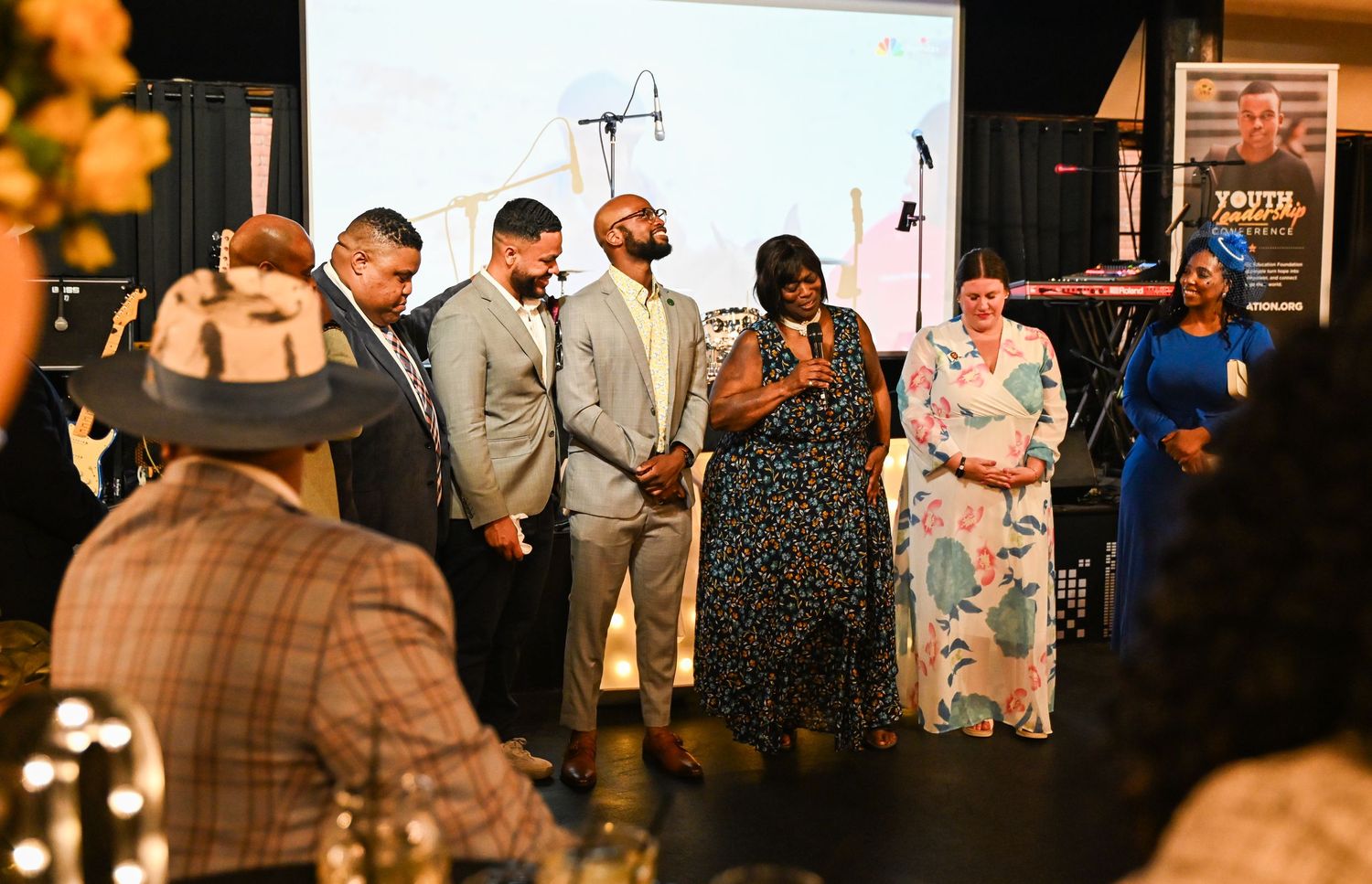 A group of people stand together on stage during an evening event with warm lighting and decorative elements.