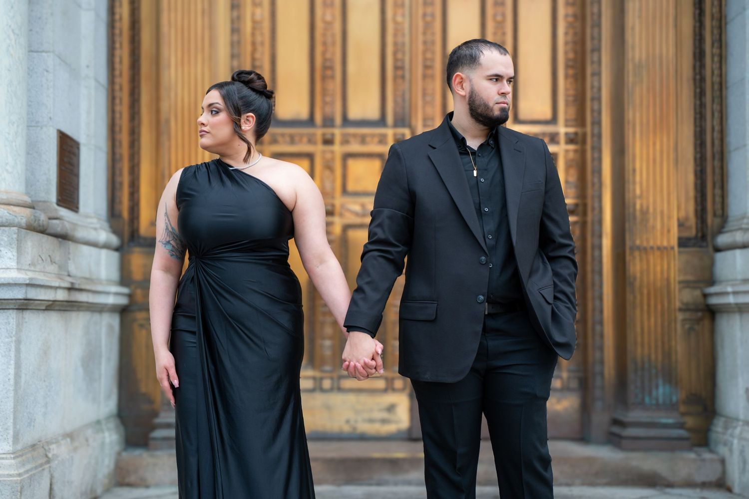 Couple in formal black attire posing in front of classical building columns.