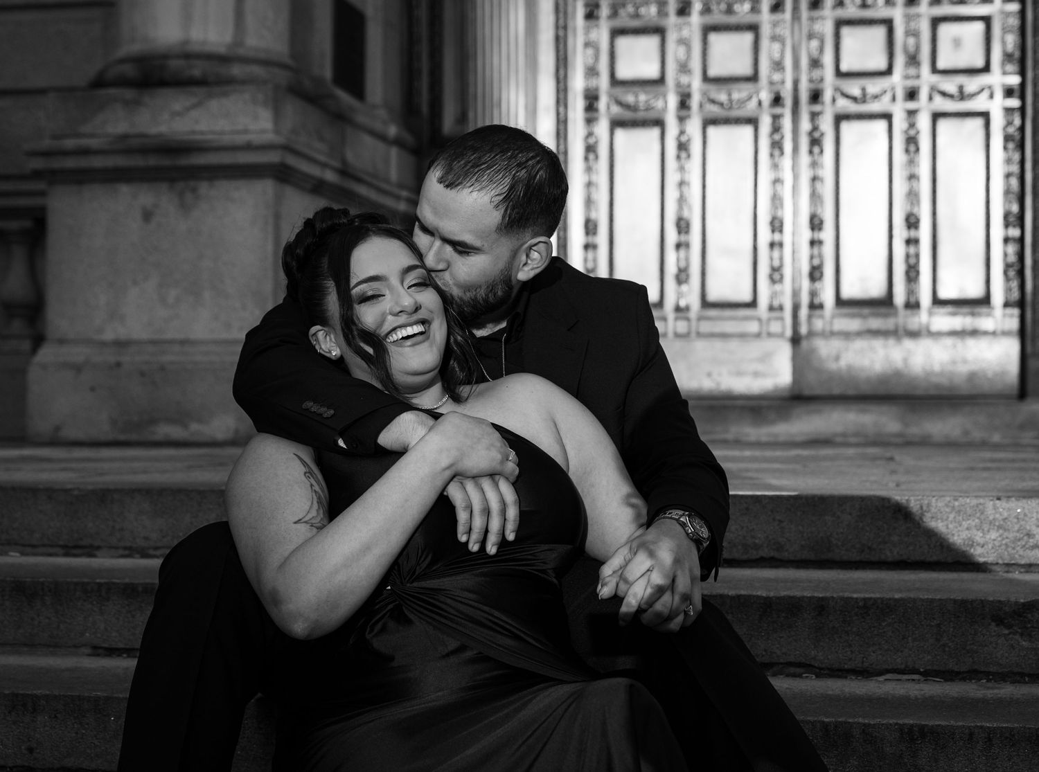 Candid black and white photo of couple laughing together on architectural steps.