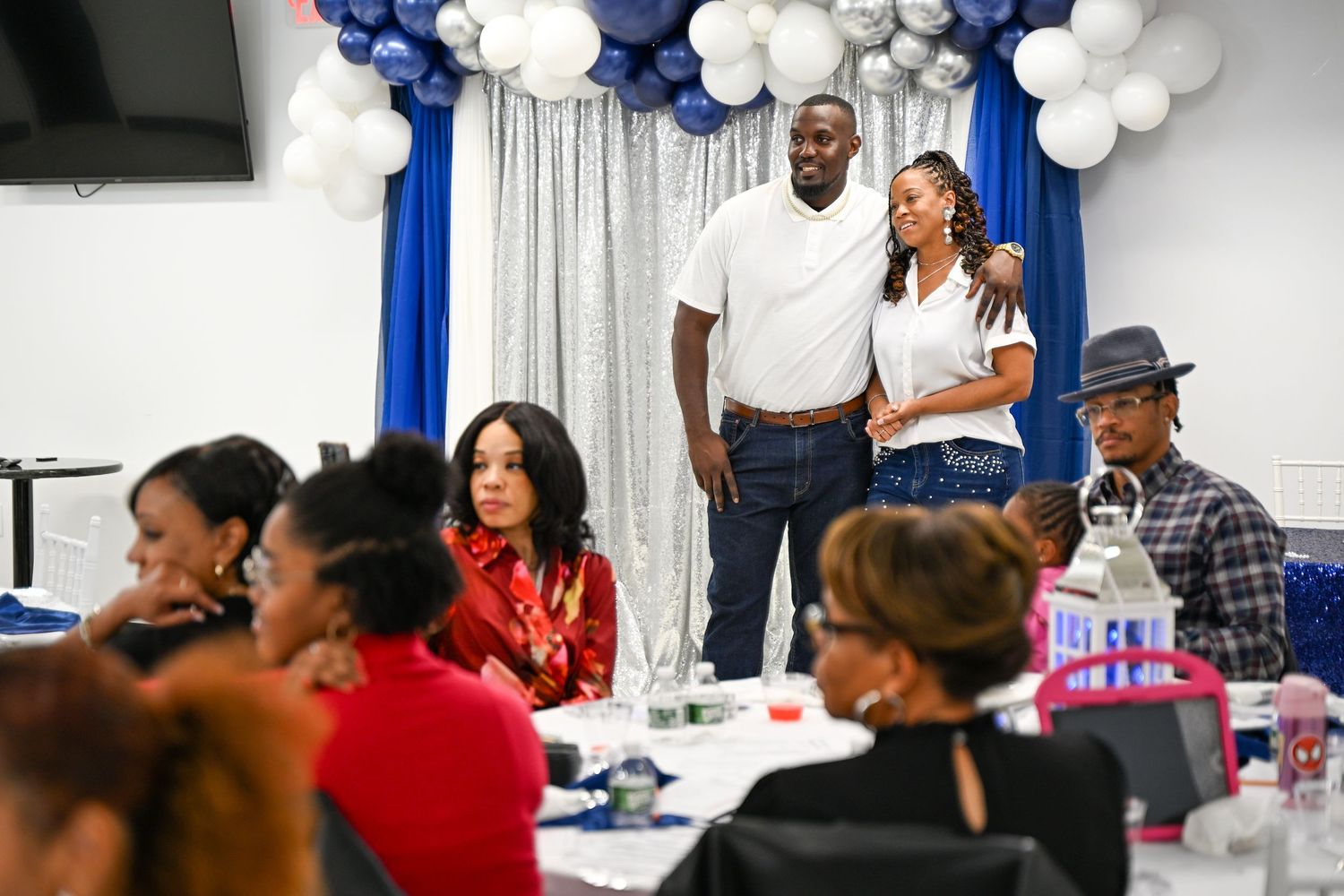 People gather at tables decorated with white and blue balloons during a celebration event.