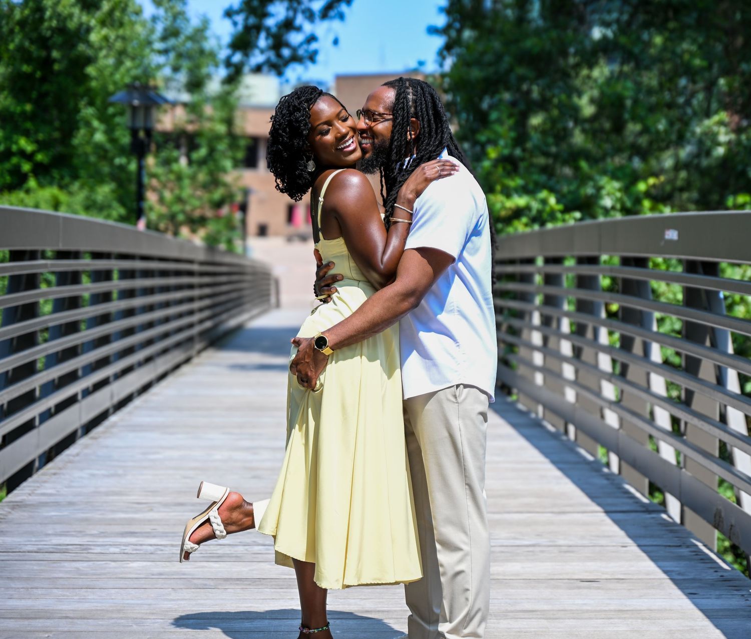 Couple sharing intimate moment on wooden boardwalk surrounded by greenery.