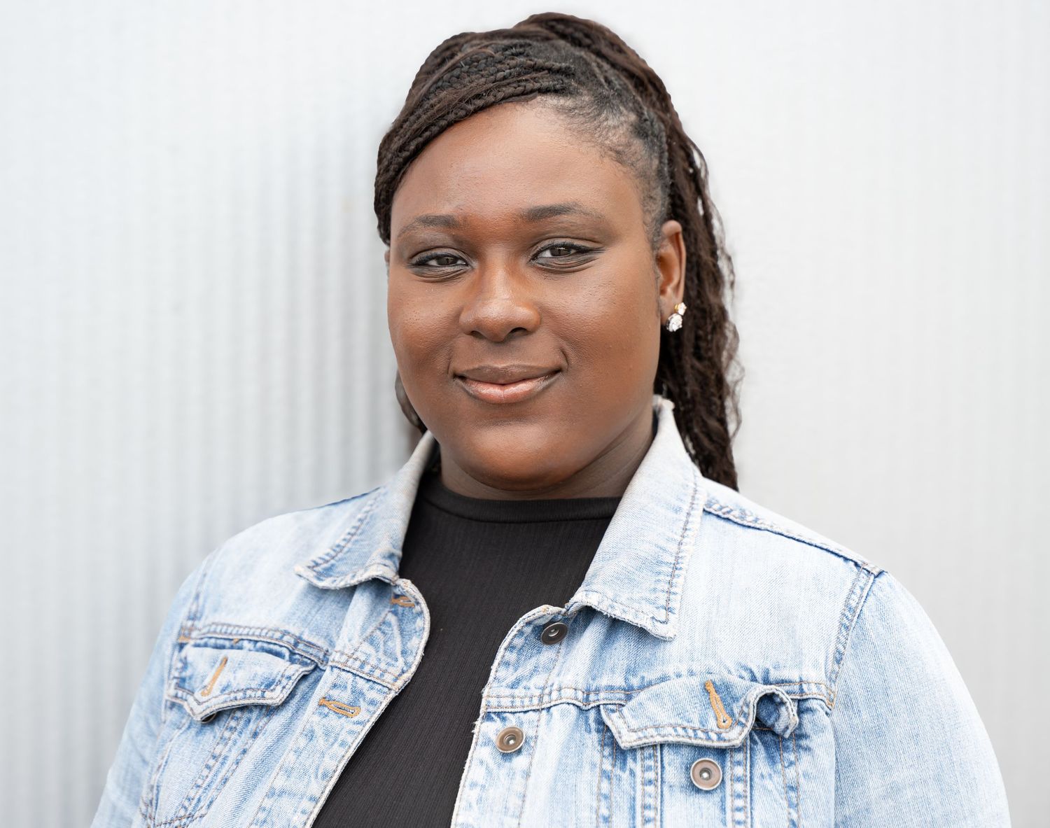 Professional portrait in a denim jacket and black top against a light background.