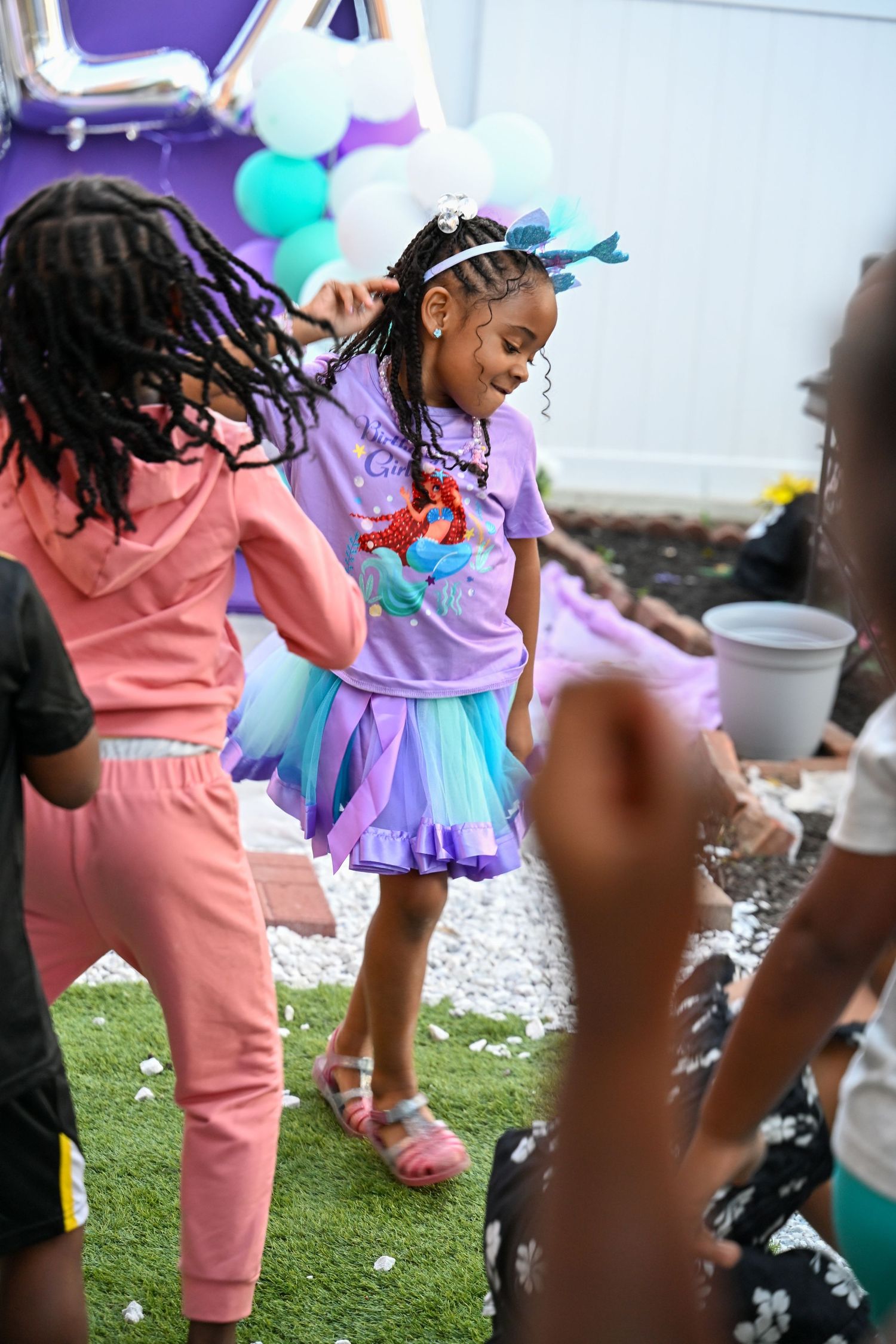 Kids in colorful outfits playing at an outdoor party with purple and teal decorations.