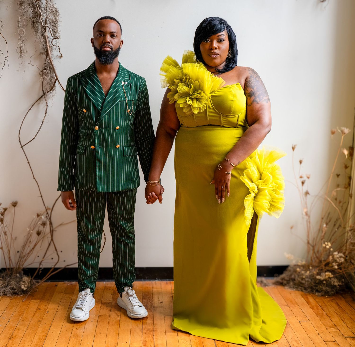 Couple poses together, one wearing a green striped suit and the other in a vibrant yellow dress with ruffles.