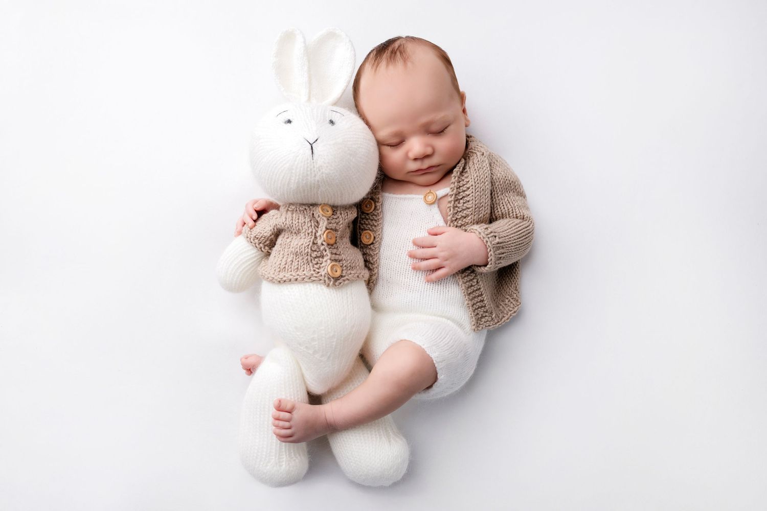 Baby dressed in light clothing resting on white bedding with stuffed toy bears.