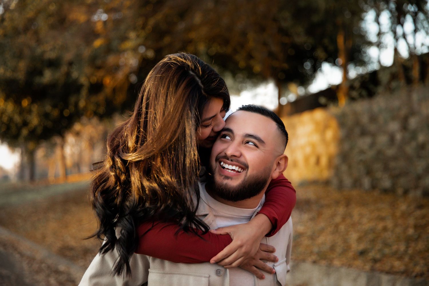 Loving couple embracing outdoors during golden hour with autumn leaves in background.