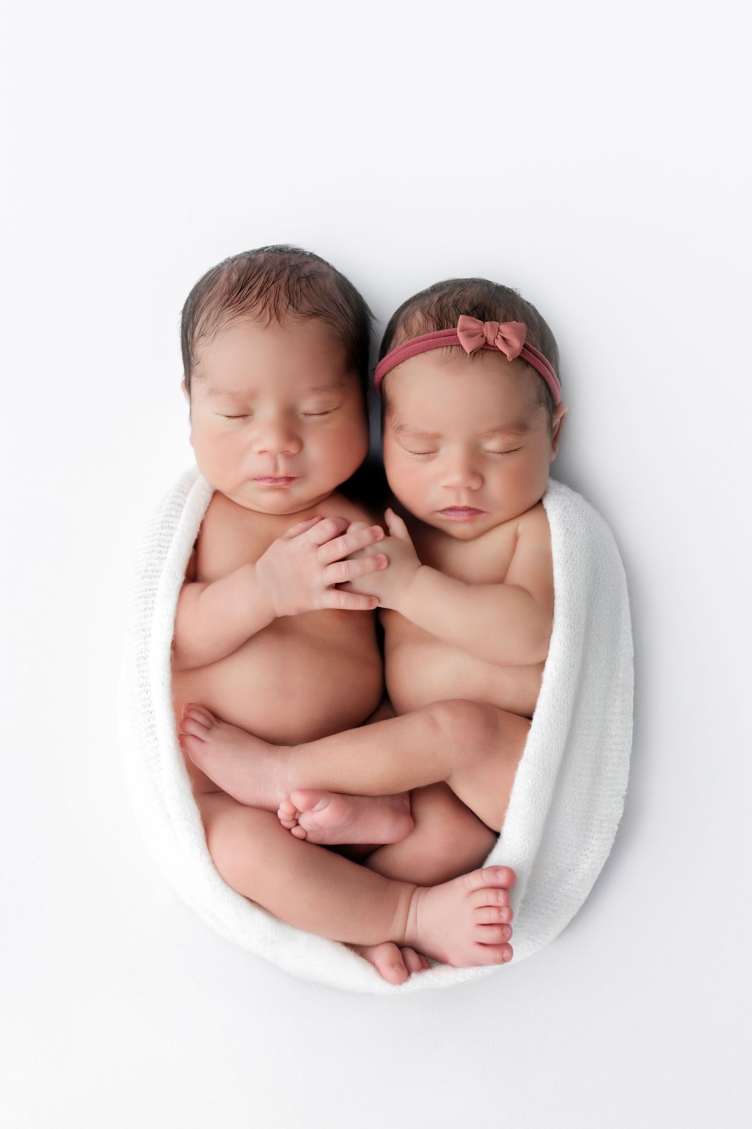 Three adorable sleeping newborn twins snuggled together, wrapped in white blankets on a light background.