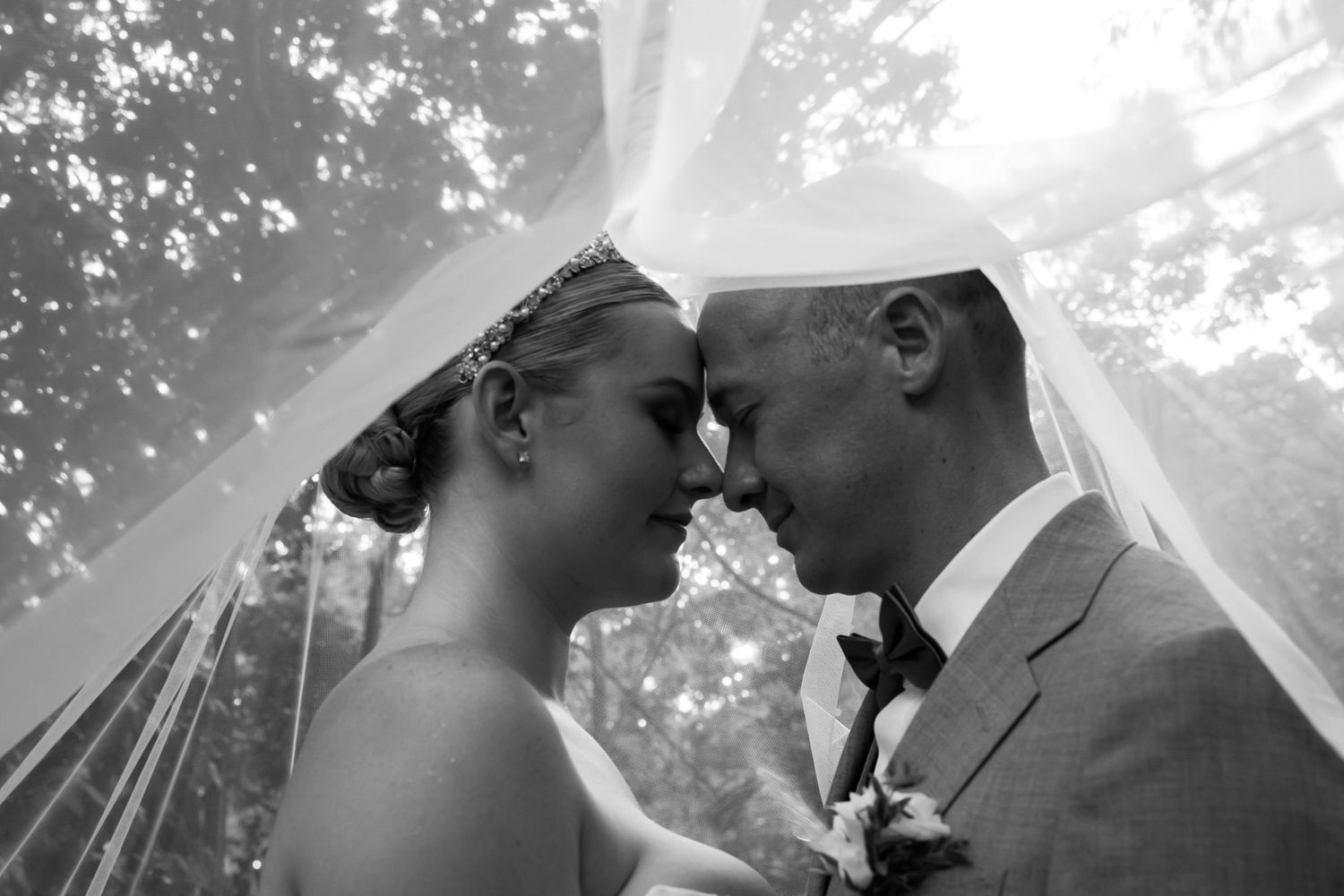 A black and white close-up of a tender moment between newlyweds under a flowing veil.