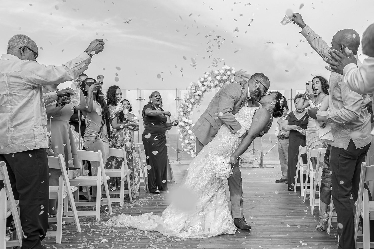 A black and white photo of guests throwing confetti during a wedding ceremony recessional.