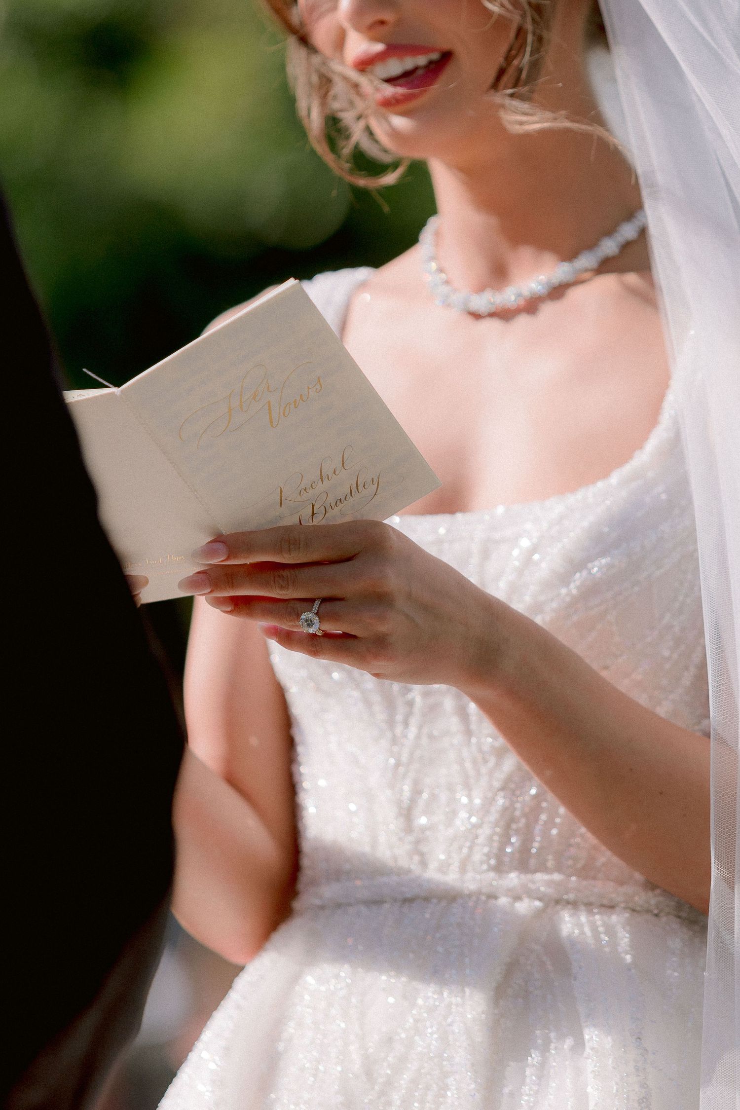 A bride in a white lace dress with pearl necklace reads a card on her wedding day.