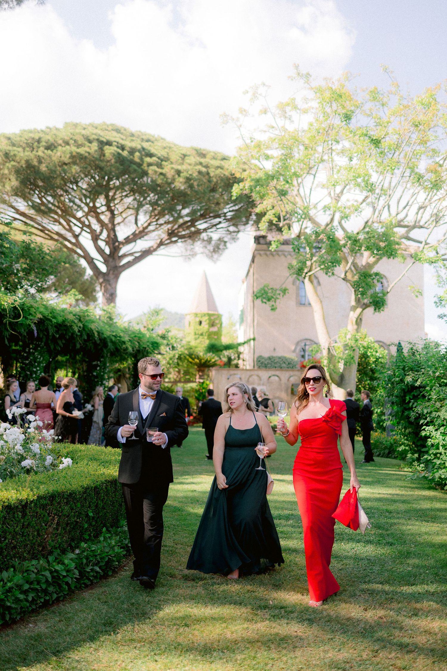 Guests in formal attire walking through a lush garden with Italian stone pine trees at an elegant outdoor event at Villa Cimbrone in Ravello