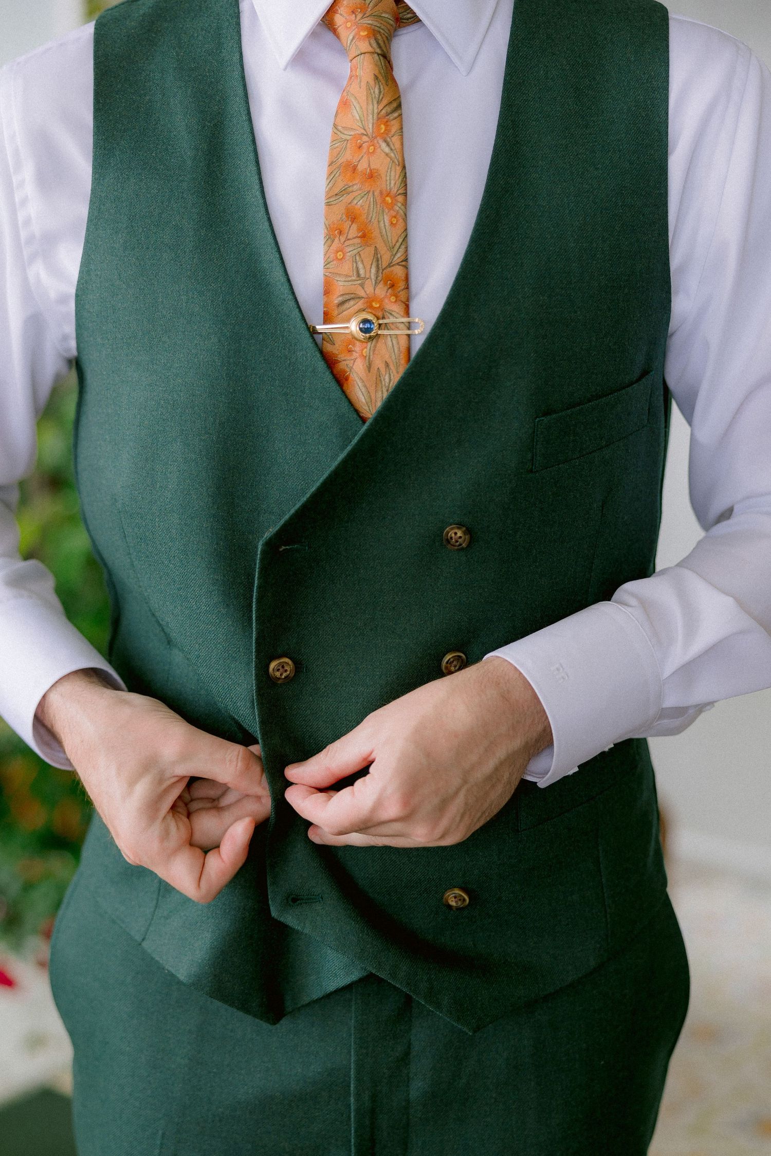 A formal outfit featuring a dark green double-breasted waistcoat paired with an orange patterned tie and white dress shirt.