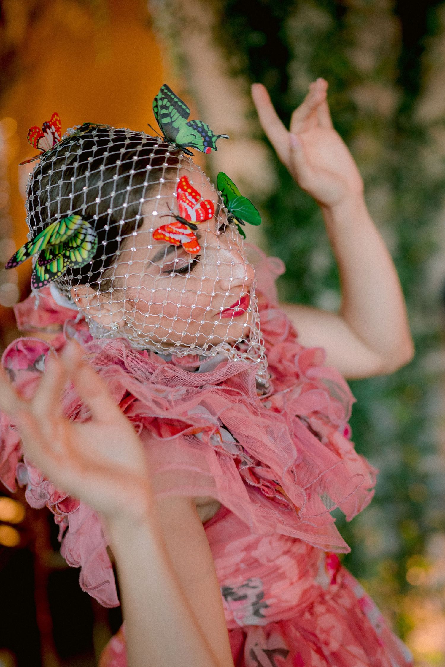 Whimsical fashion photo featuring pink ruffled dress, netted veil and decorative butterflies in green and red tones.