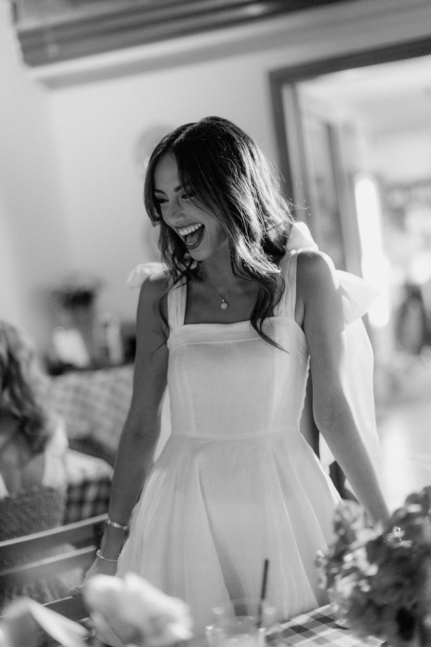 A joyful woman in a white dress laughs heartily in a candid black and white photograph.