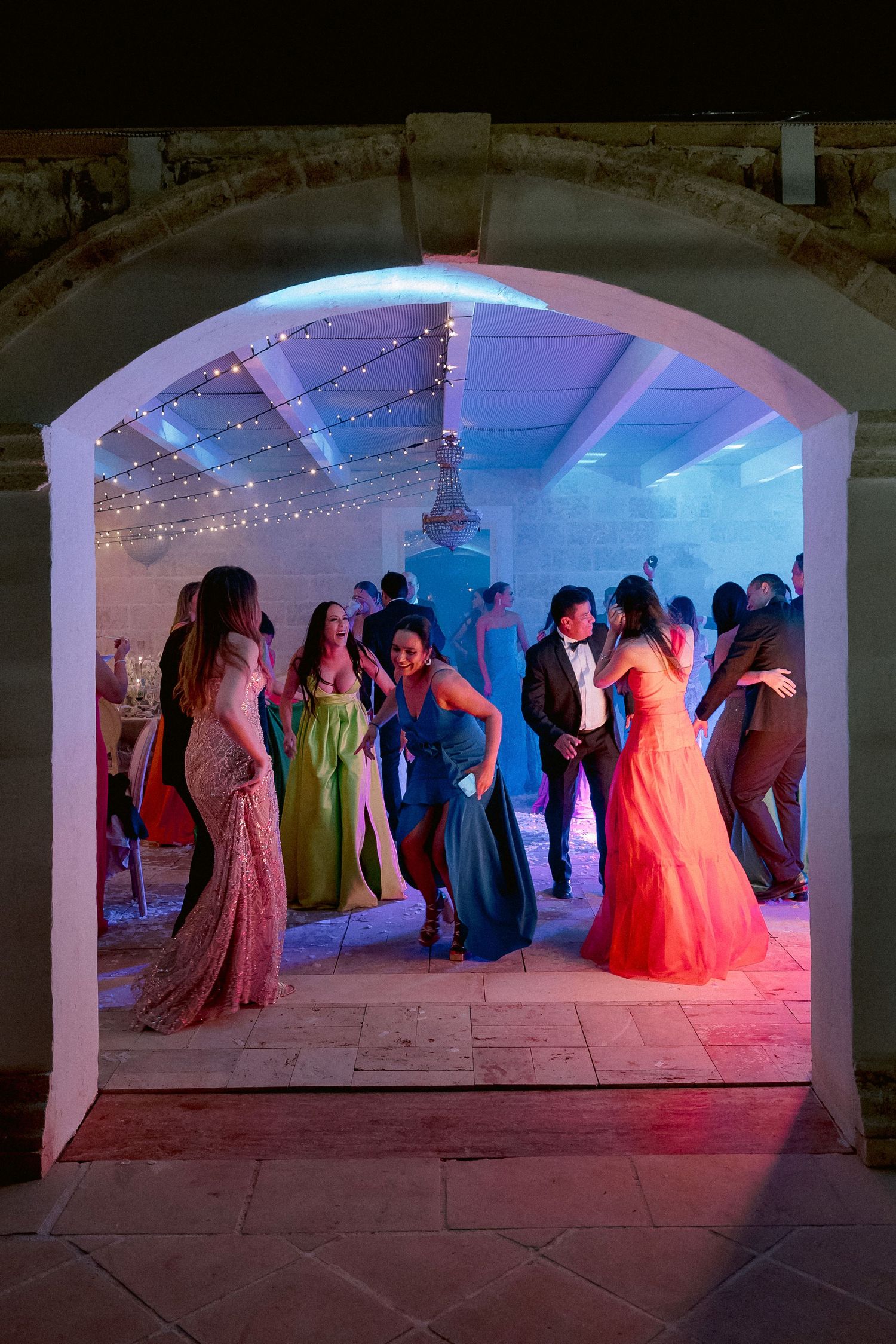 People dancing at a formal event under an illuminated archway with colorful pink and blue lighting.