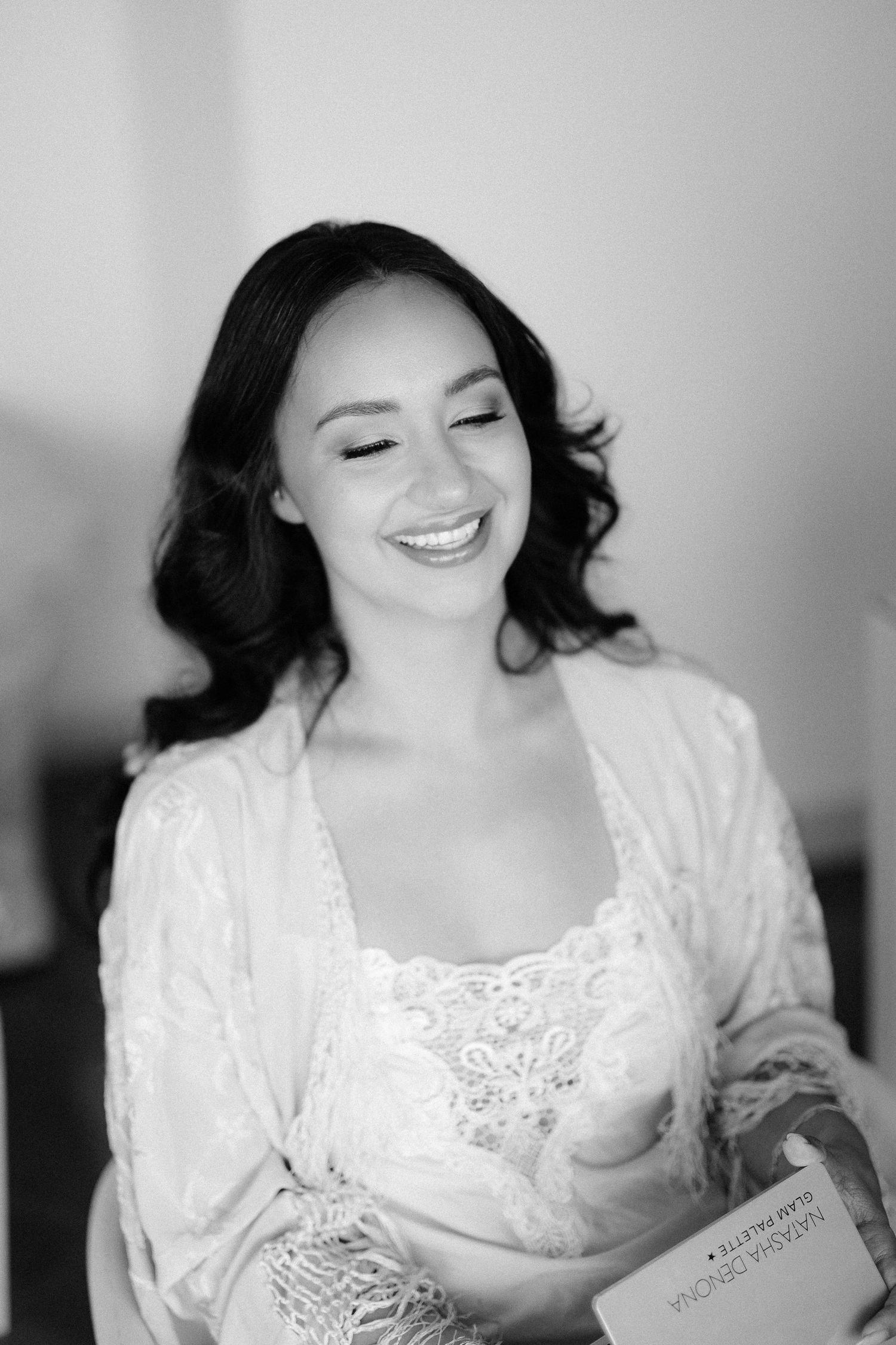 Black and white portrait of woman in white lace robe smiling while reading, with soft lighting and natural expression.