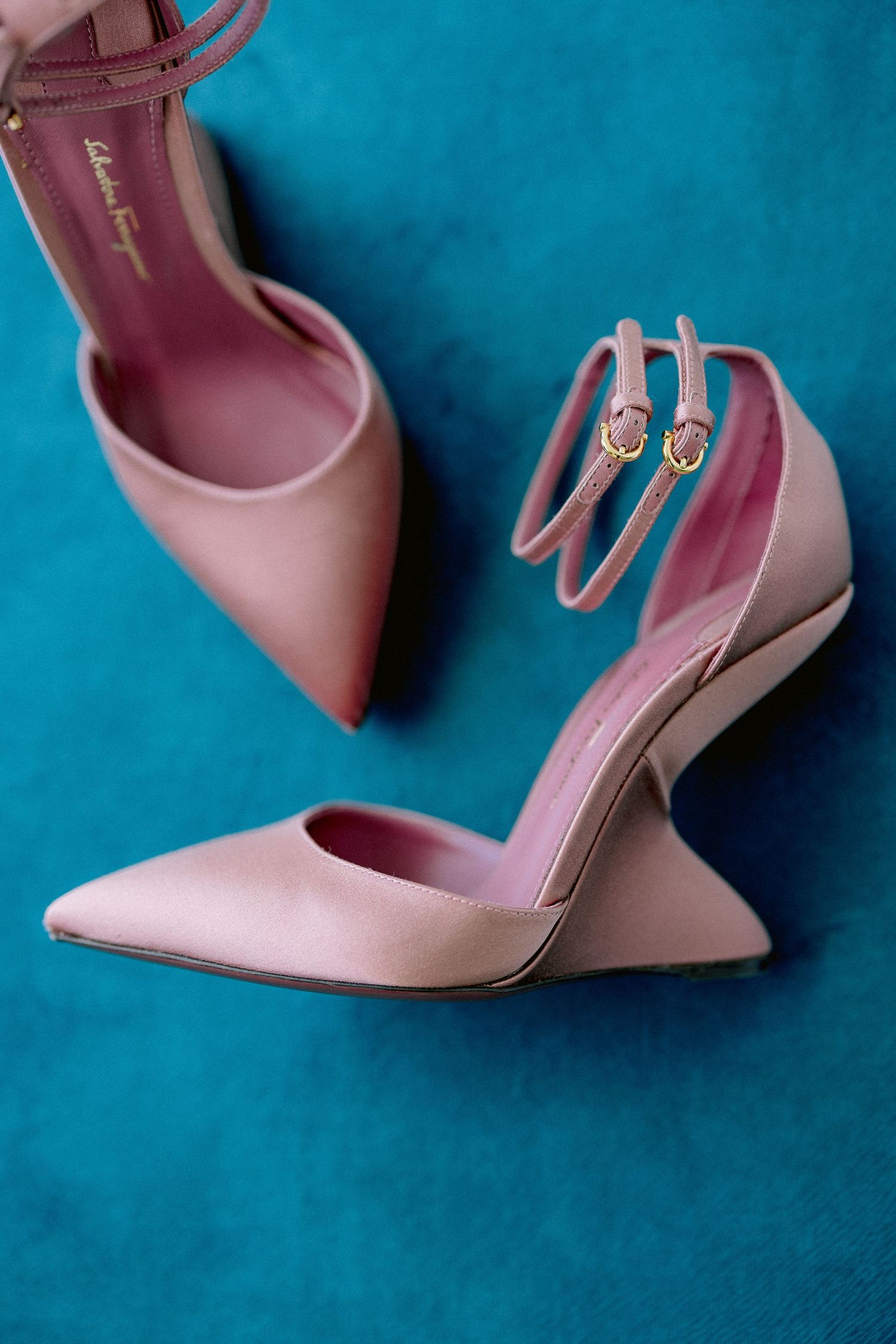 Elegant pink pointed-toe heels with ankle straps photographed against a vibrant turquoise background.
