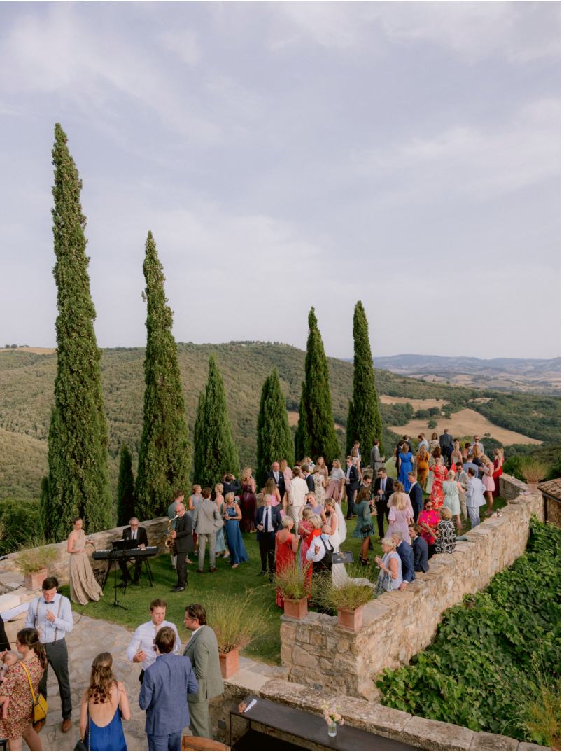 Outdoor wedding reception on a Tuscan terrace with cypress trees and rolling hills in the background.