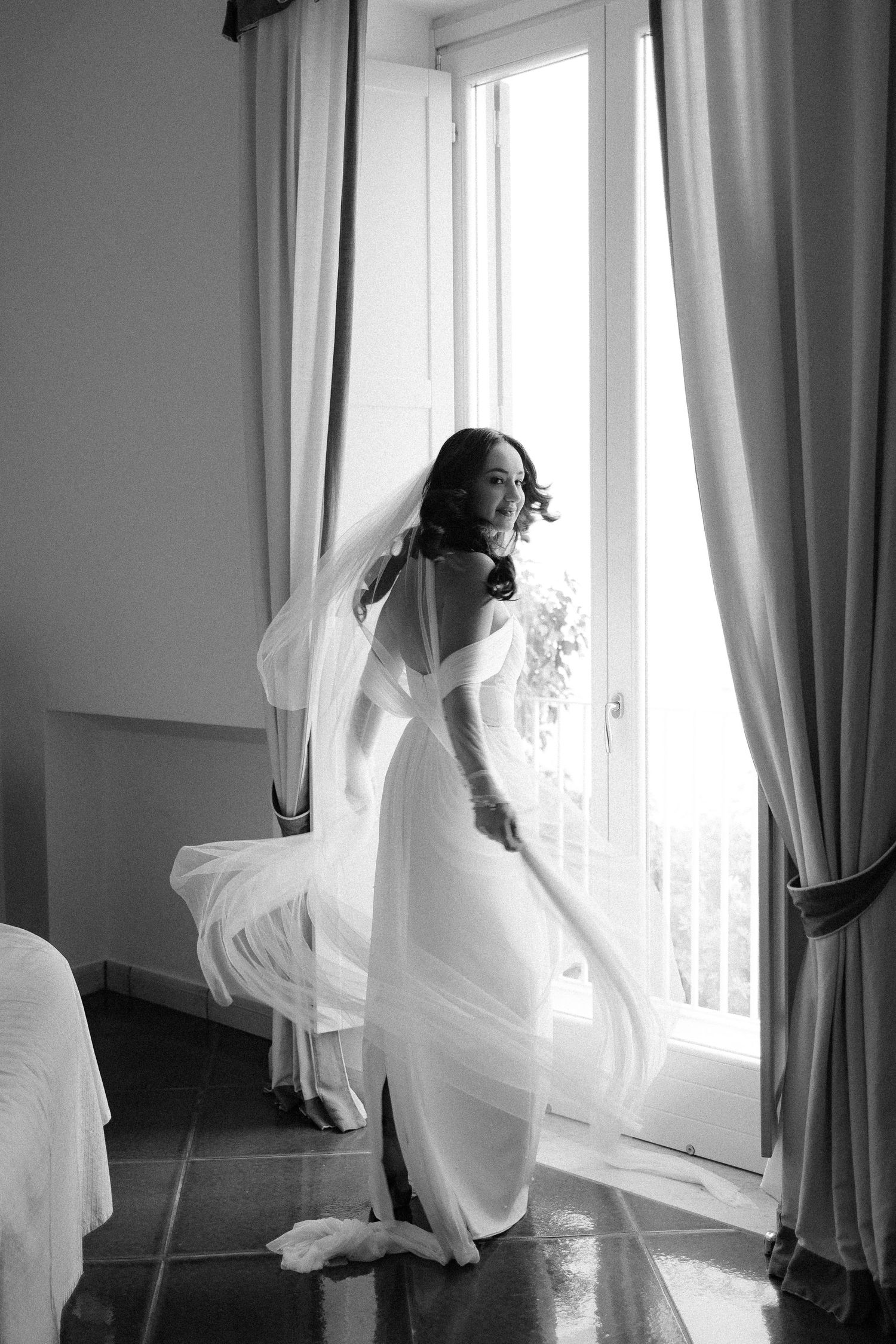 A graceful figure in a flowing white dress dances and twirls by a sunlit window with billowing curtains.