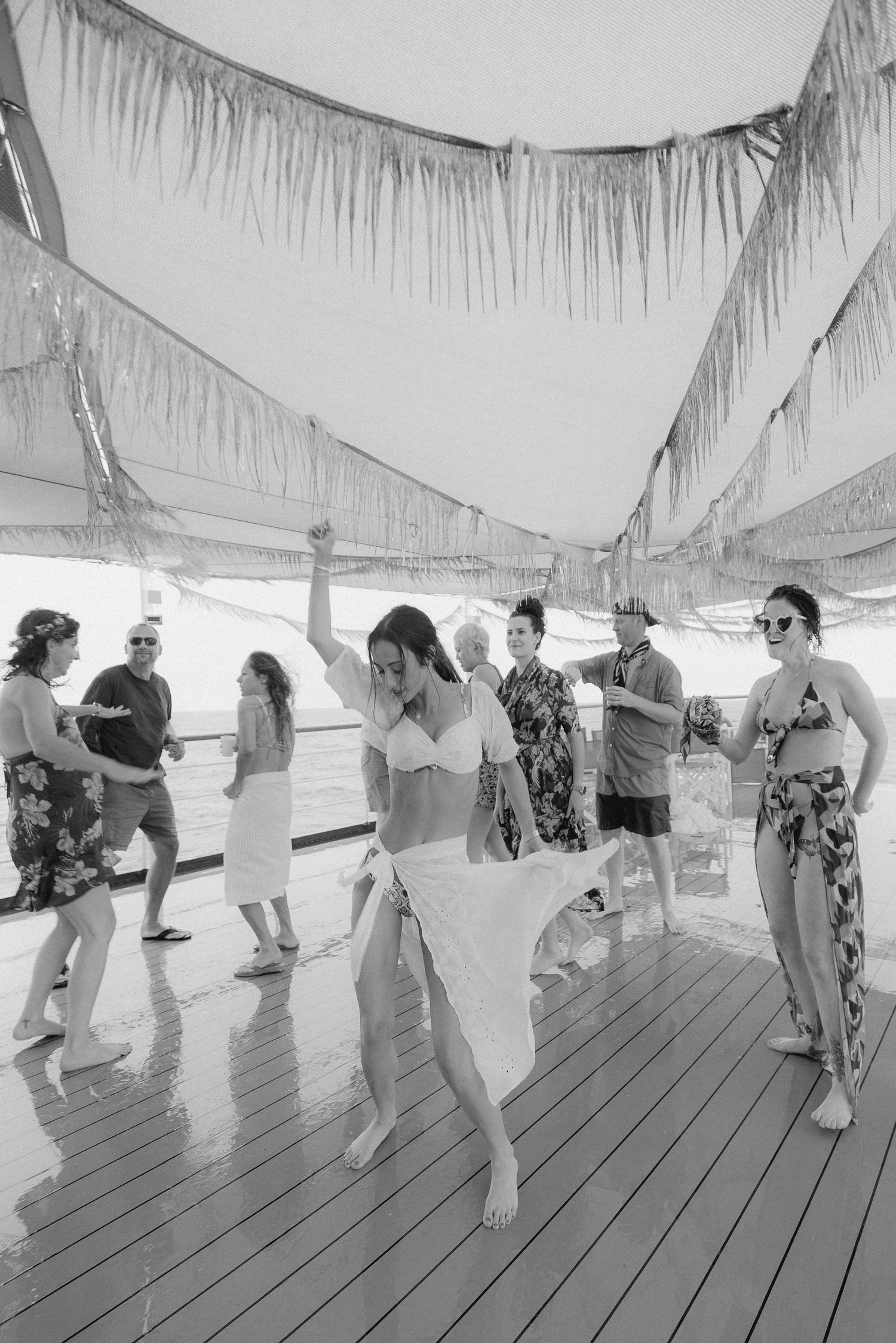 A group of people dancing and celebrating on a covered wooden deck at a summer party.