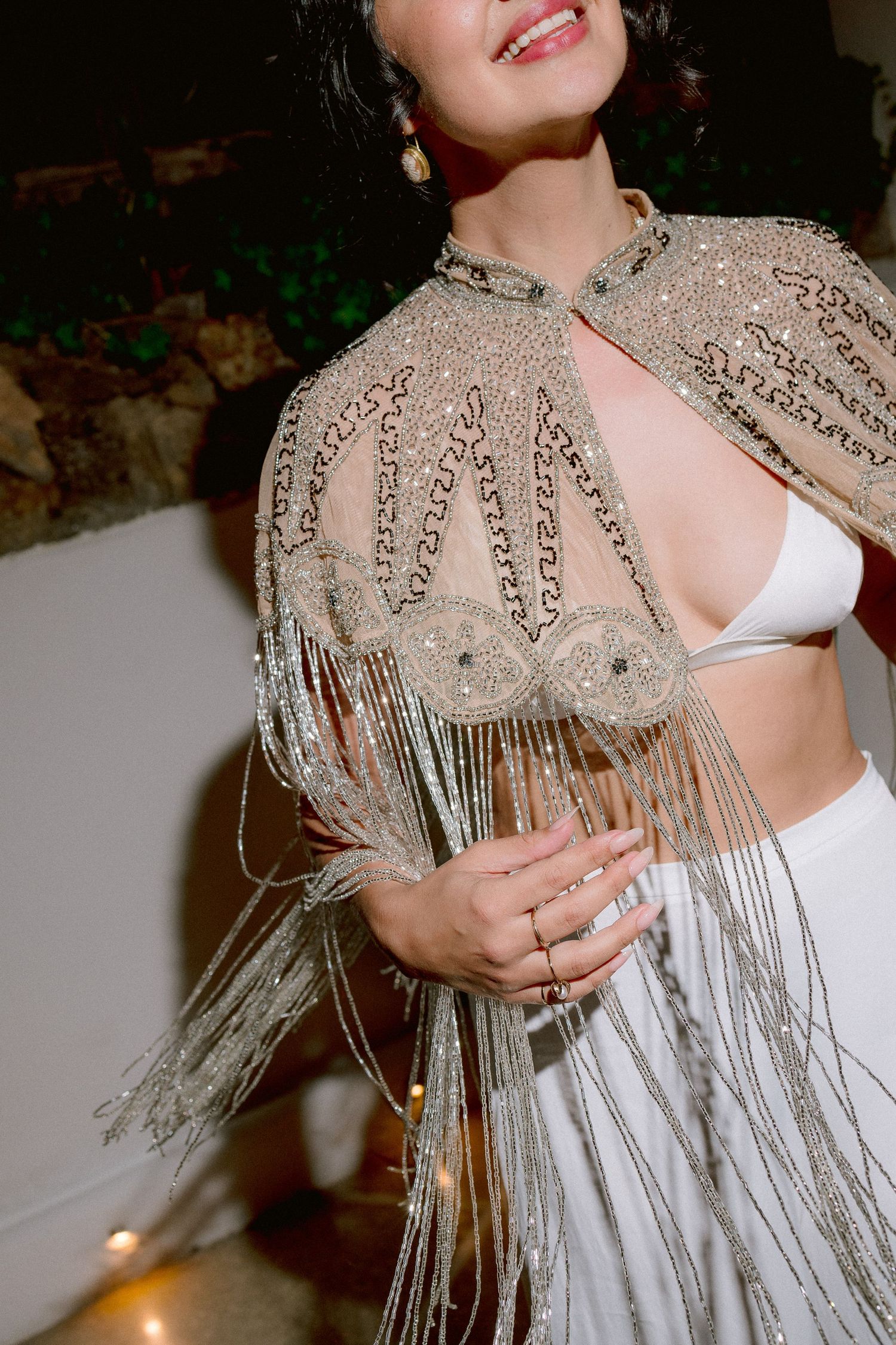 Close-up of an intricately beaded silver capelet with long fringe tassels worn over white undergarments.