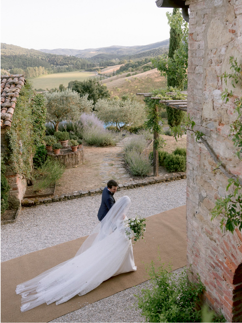 Bride and groom share a romantic moment in a Tuscan villa garden with rolling hills and lush greenery backdrop.