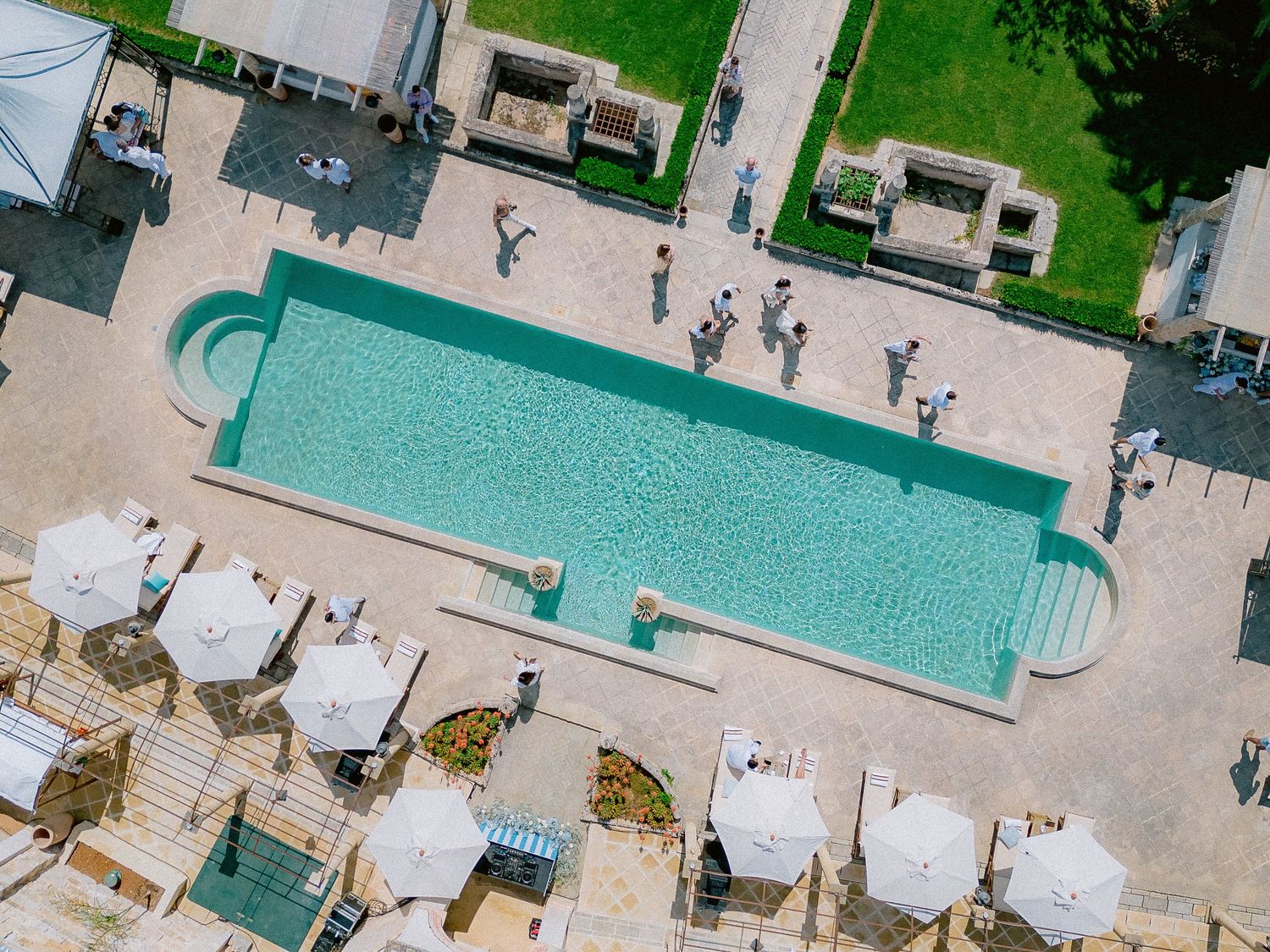 Aerial view of Tenuta San Mose pool with white cabanas and lounge chairs on a stone deck surrounded by green landscaping.