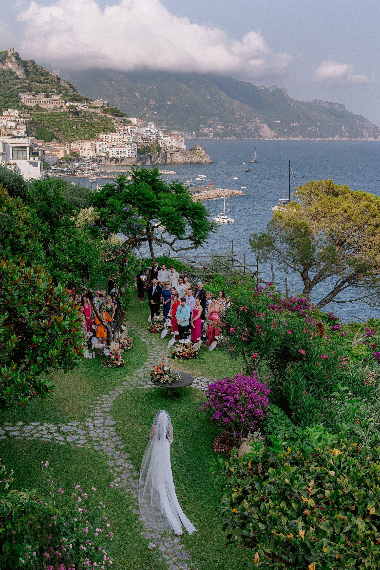 A scenic wedding ceremony on a garden terrace overlooking the Amalfi Coast with mountains and Mediterranean Sea views.
