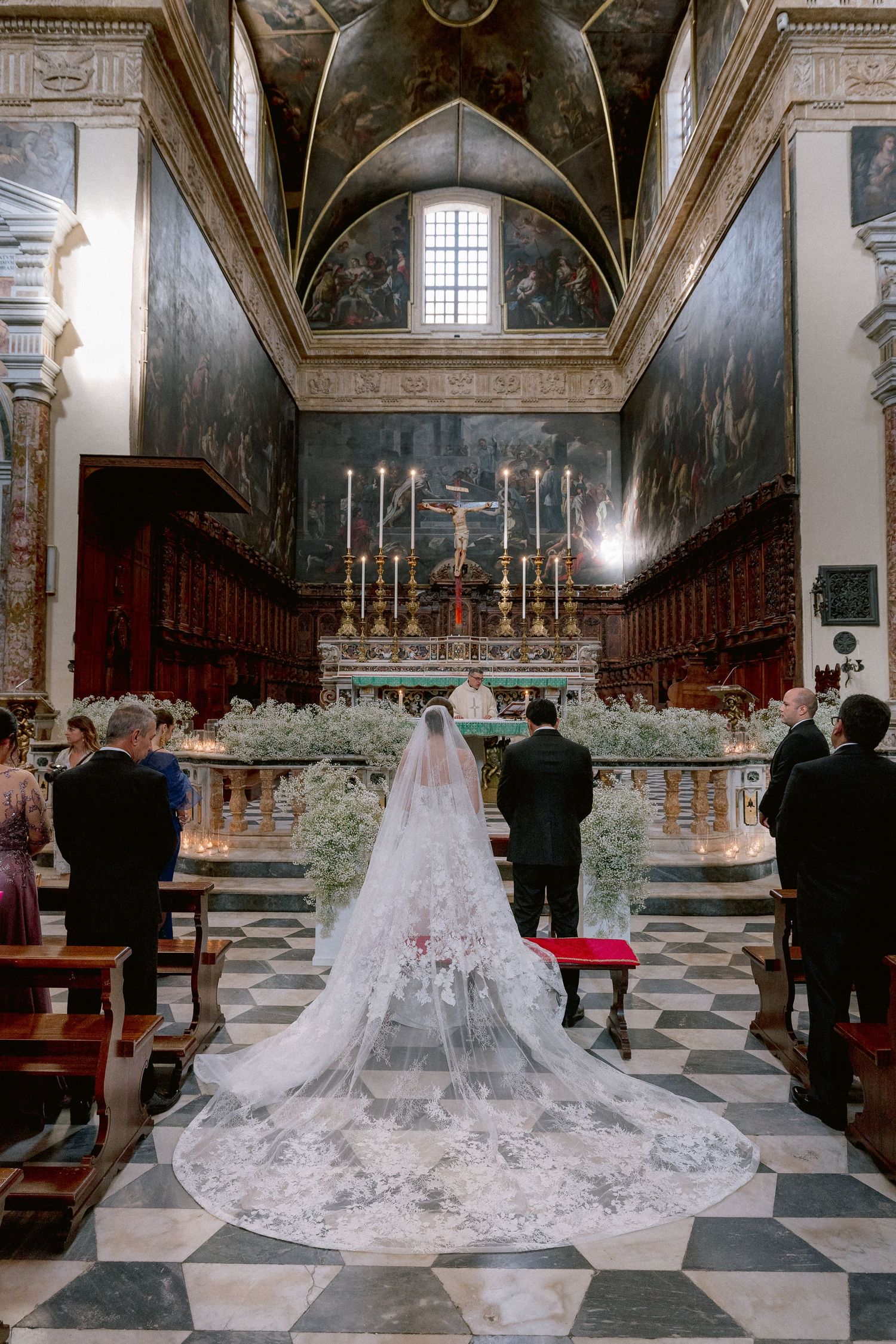 A cathedral wedding ceremony with a long lace veil trailing down the black and white checkered floor.