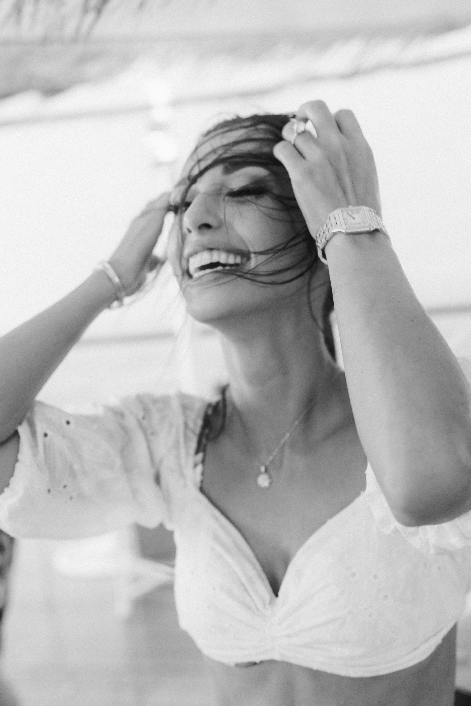 Black and white portrait of a joyful person in a white dress laughing while running fingers through windswept hair.