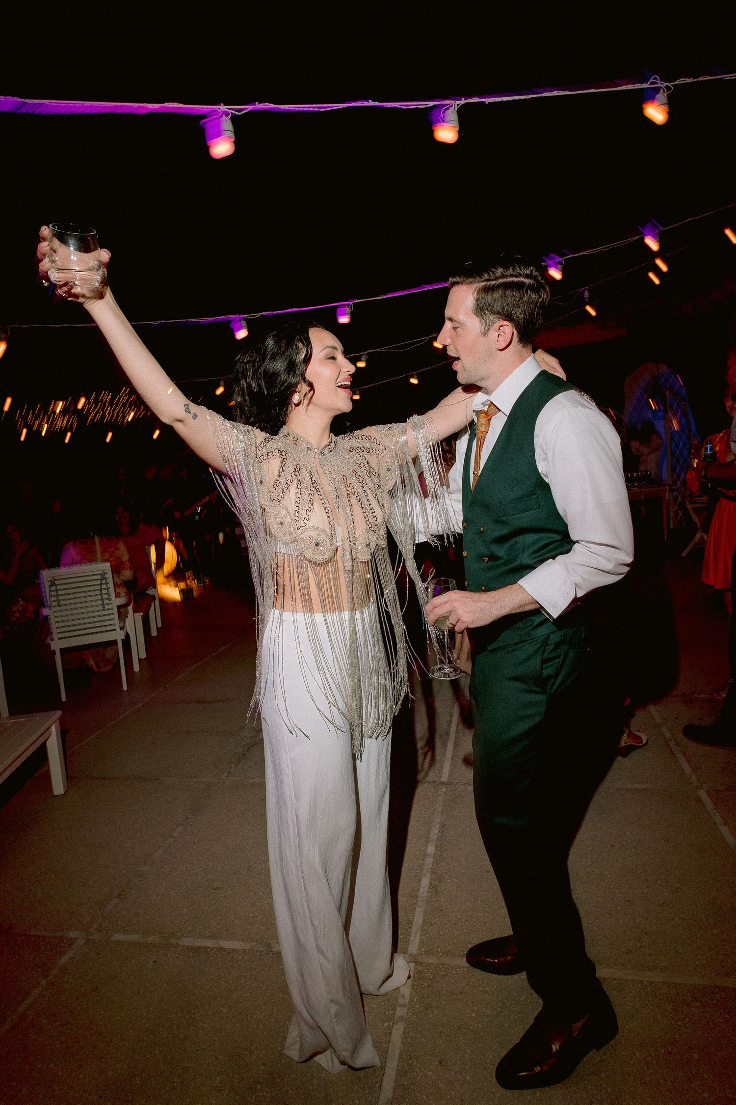 A couple dances together at a nighttime celebration under purple string lights.