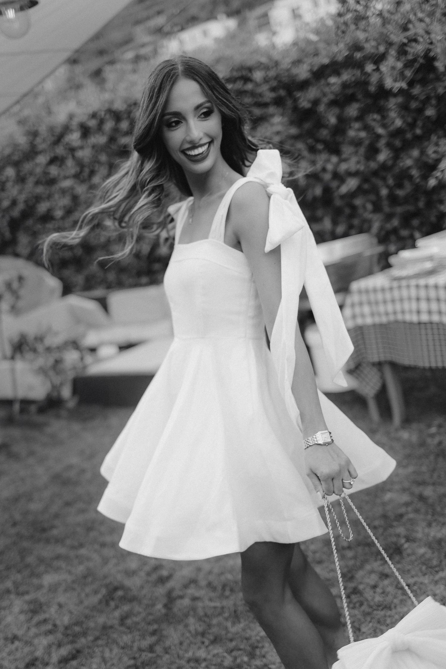 A person in a white summer dress twirls playfully outdoors in a black and white photograph.