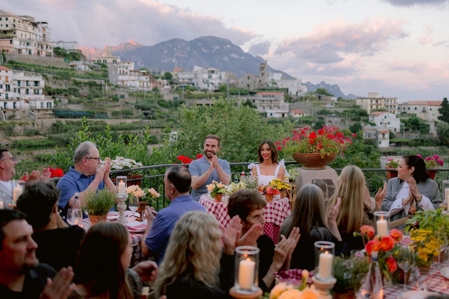 Diners enjoy an outdoor feast at a restaurant terrace overlooking the hillside homes of Amalfi Coast at sunset.