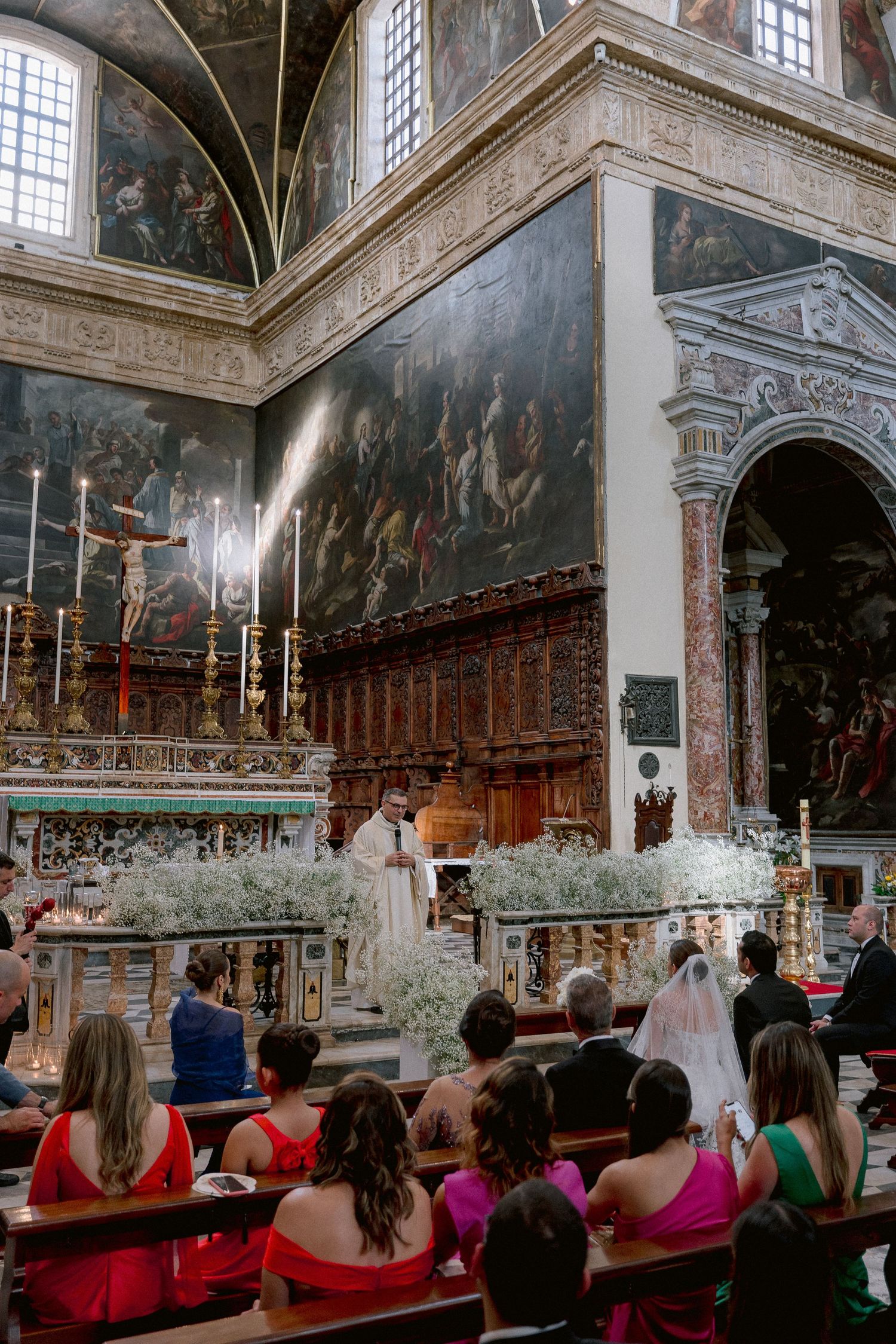 Historic Sant'Agata church in Gallipoli interior with ornate artwork and wooden choir stalls during a ceremony with floral decorations.
