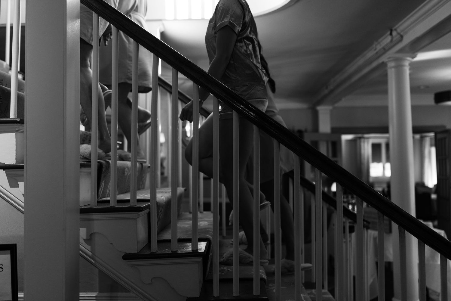 Black and white photograph of a dimly lit hallway with stairs and railings creating dramatic shadows and perspective.