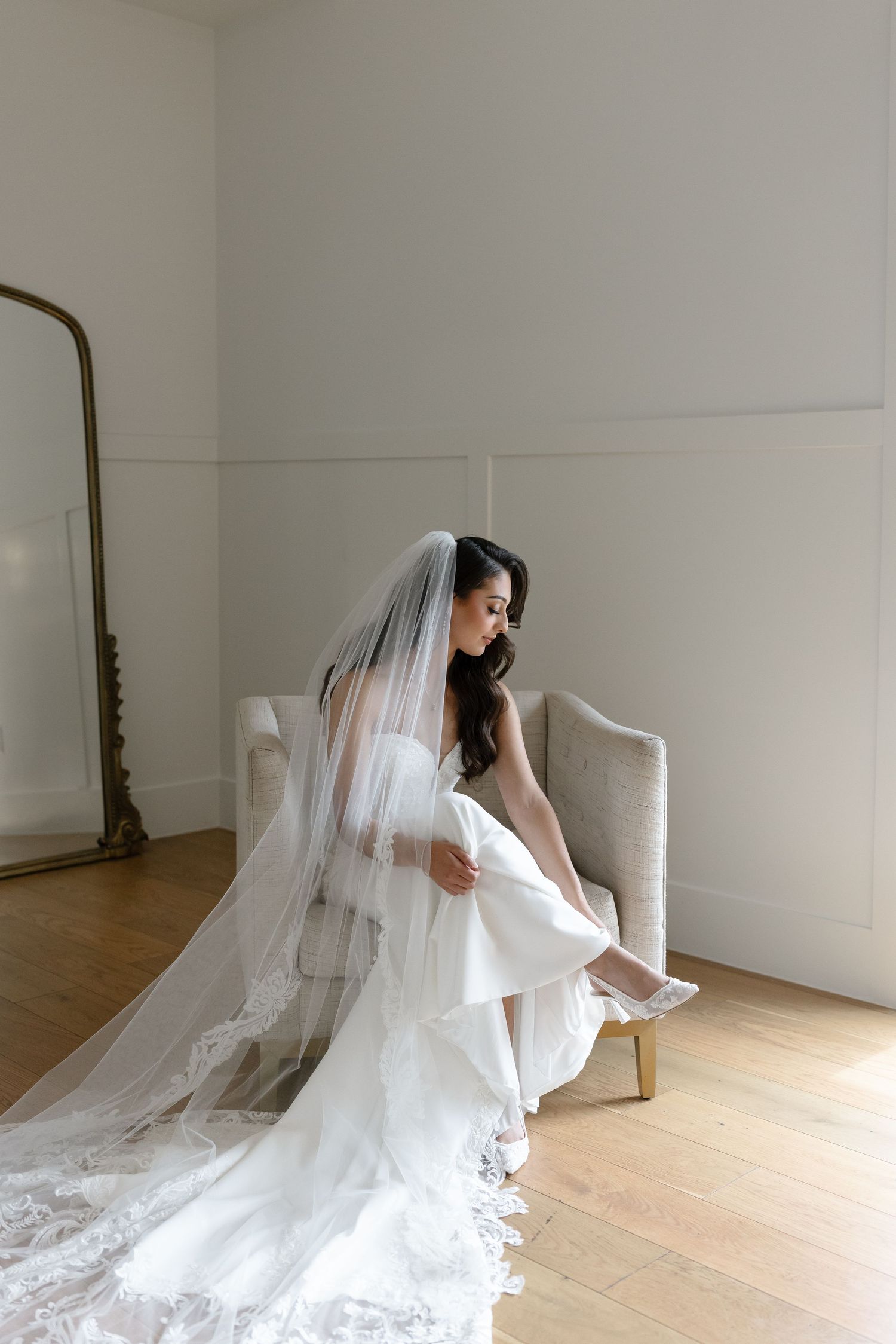 A bride in a flowing white wedding gown and veil poses gracefully in a minimalist white studio space.
