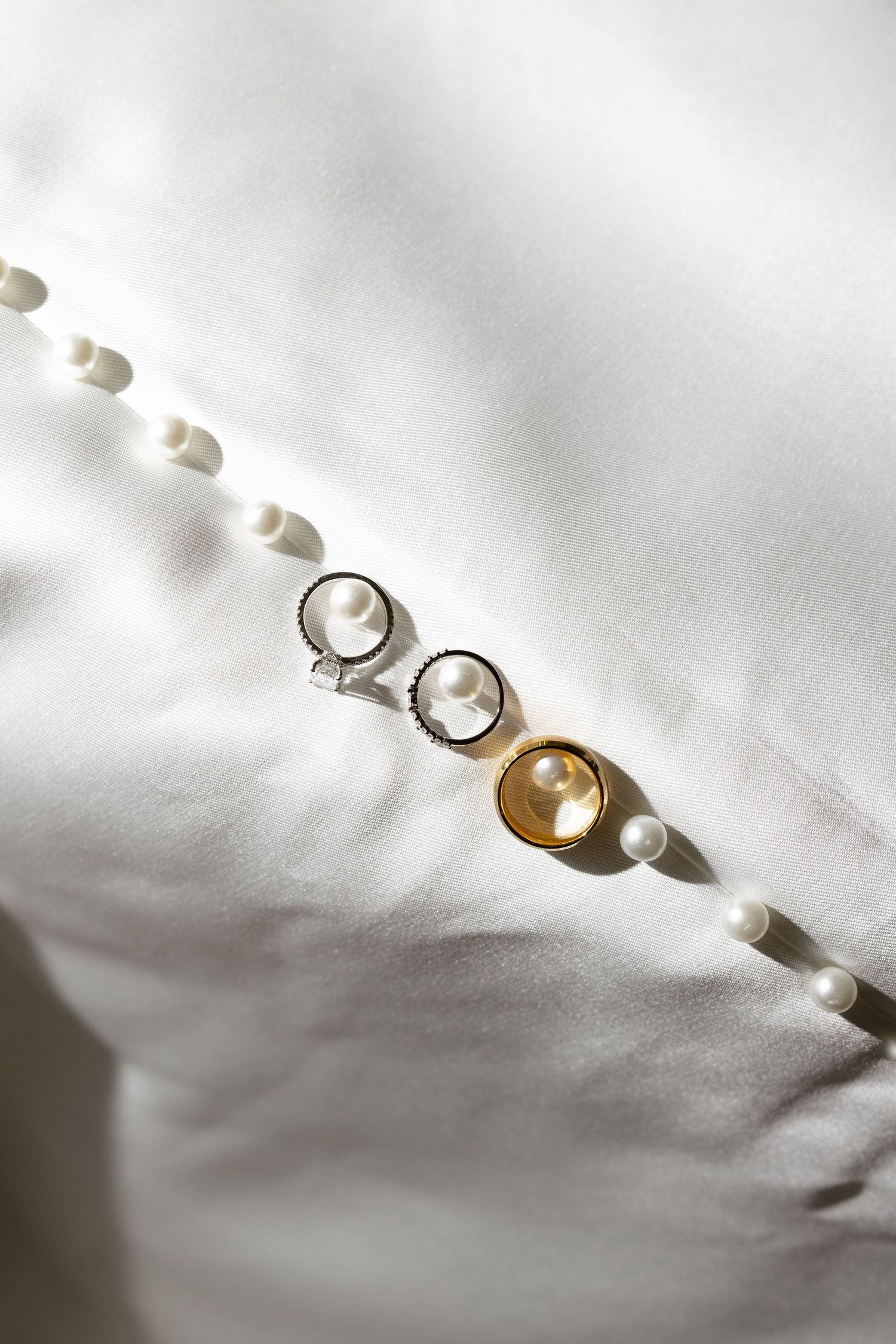 Multiple pearl stud earrings casting dramatic shadows on white fabric in a minimalist jewelry product photography series.