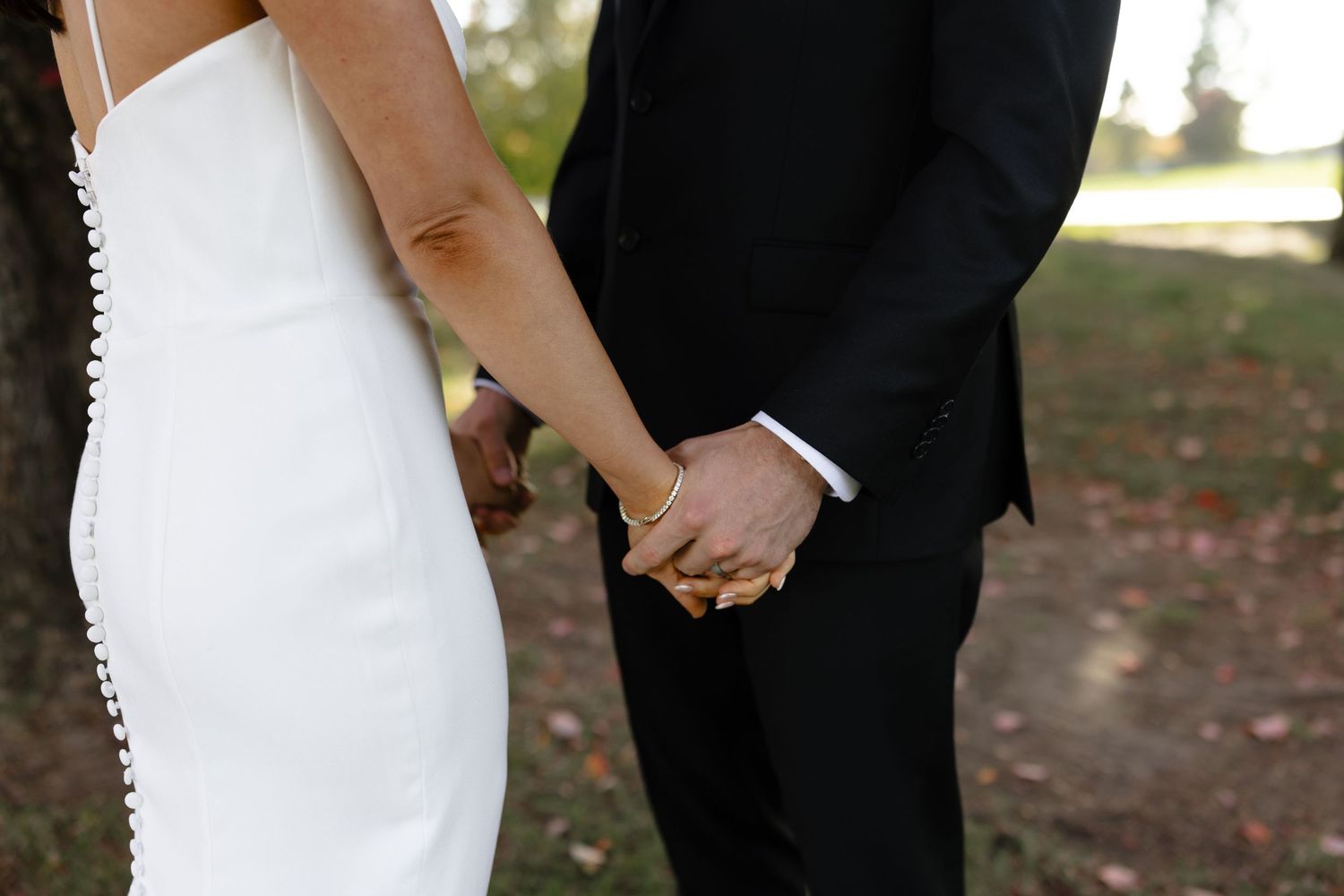A bride and groom hold hands during their outdoor wedding ceremony surrounded by autumn trees.