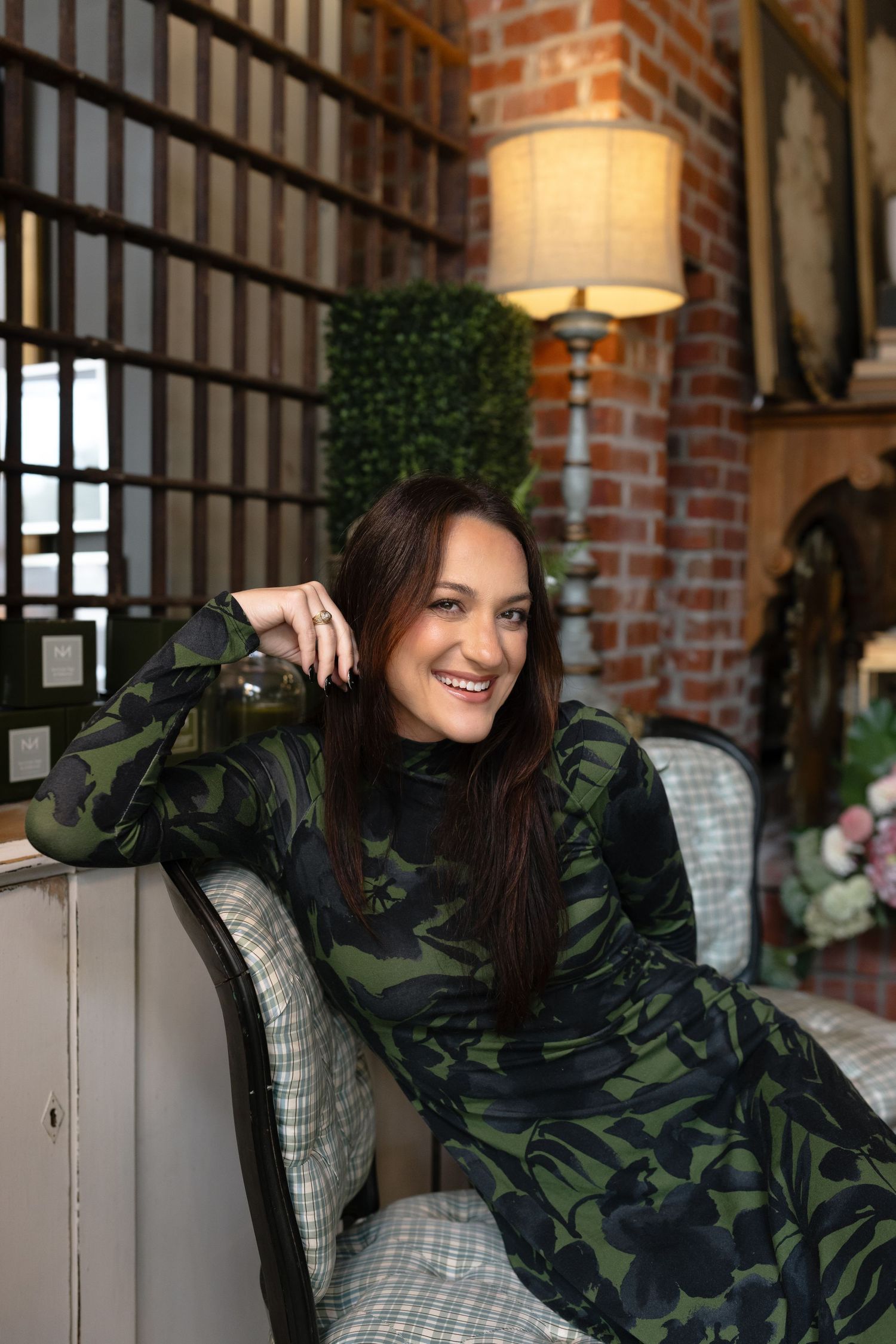 A person in a camouflage jacket poses playfully on a couch against exposed brick walls in an industrial-style space.