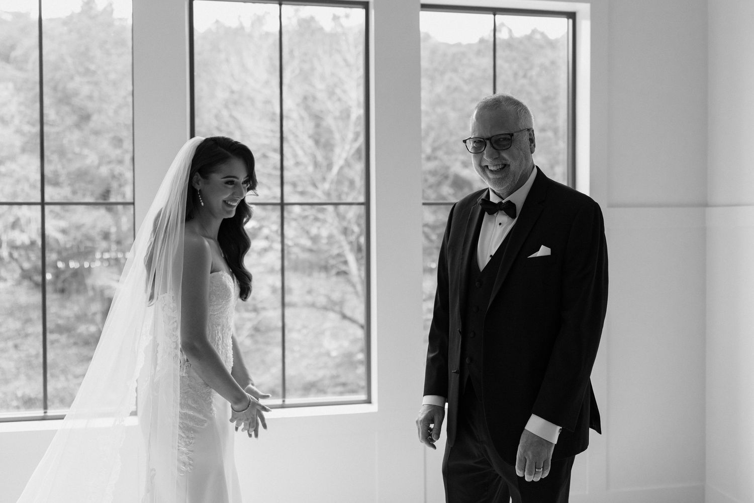 Black and white wedding photo series showing joyful moments between newlyweds in a bright, window-lit venue.