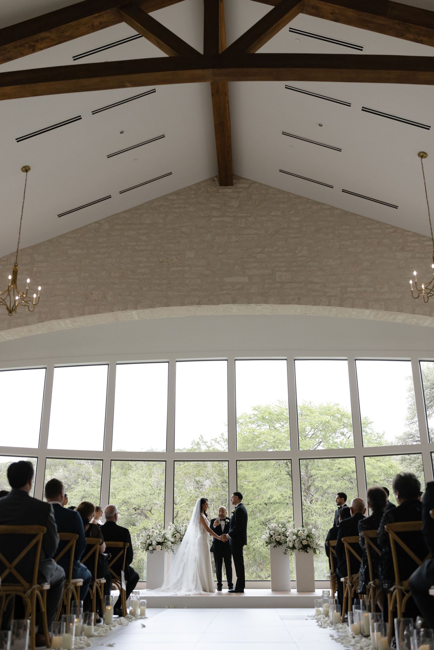 Wedding ceremony in a modern chapel with exposed wooden beams and large windows overlooking nature.