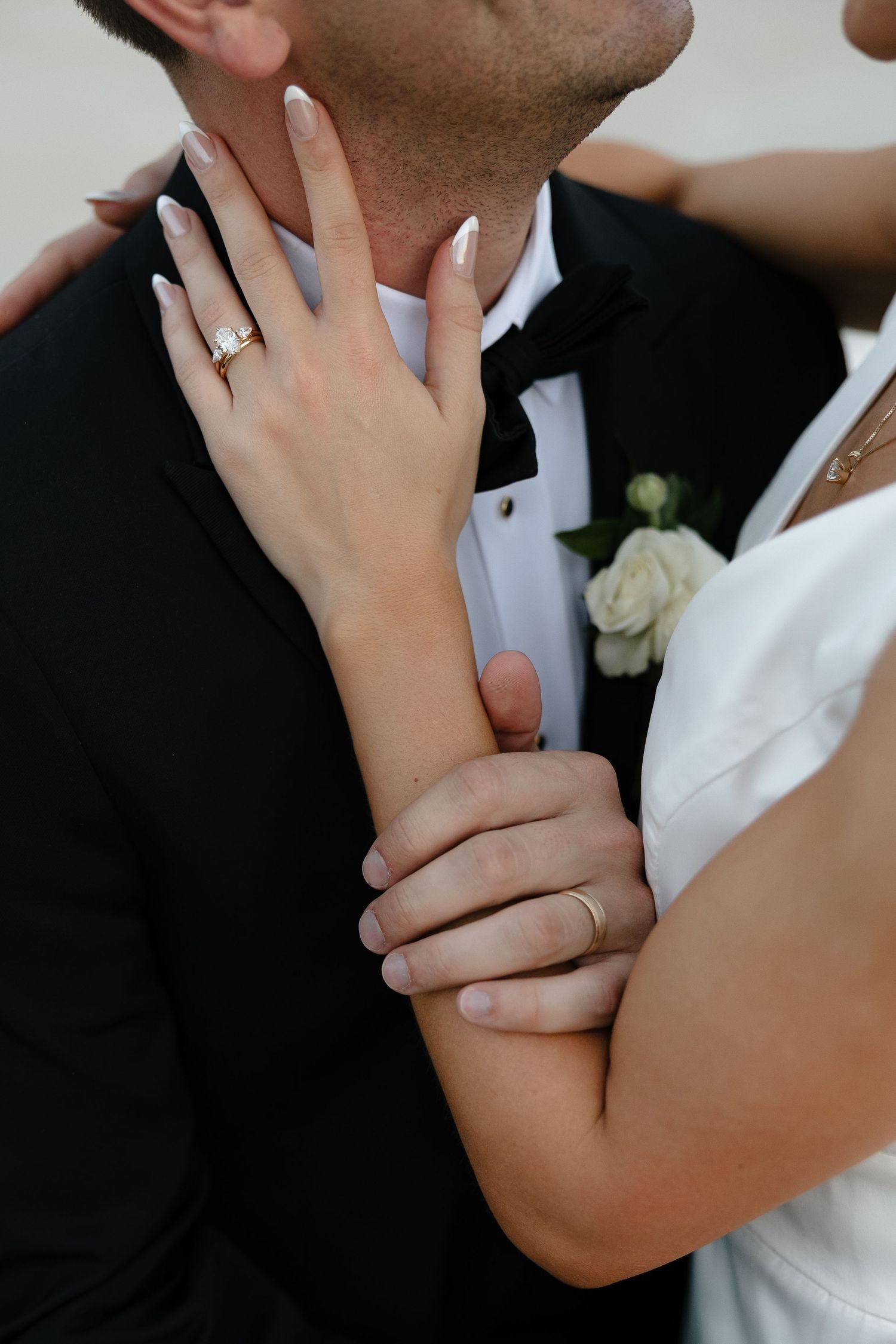 Close-up shot of newlywed couple embracing with bride's hand showing engagement ring and wedding band details.